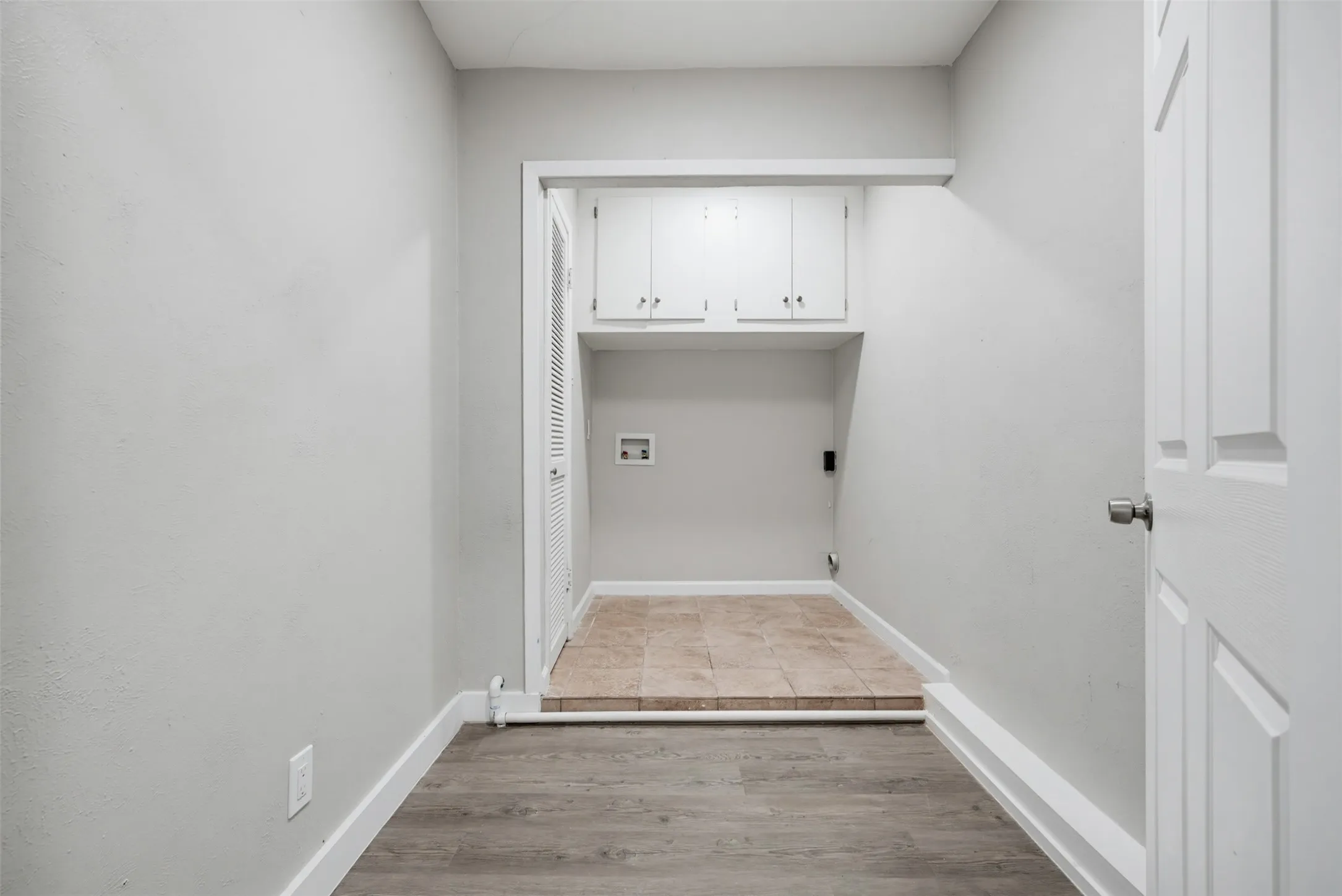 Laundry area with built-in cabinetry, ceramic tile flooring, and wood-finish flooring