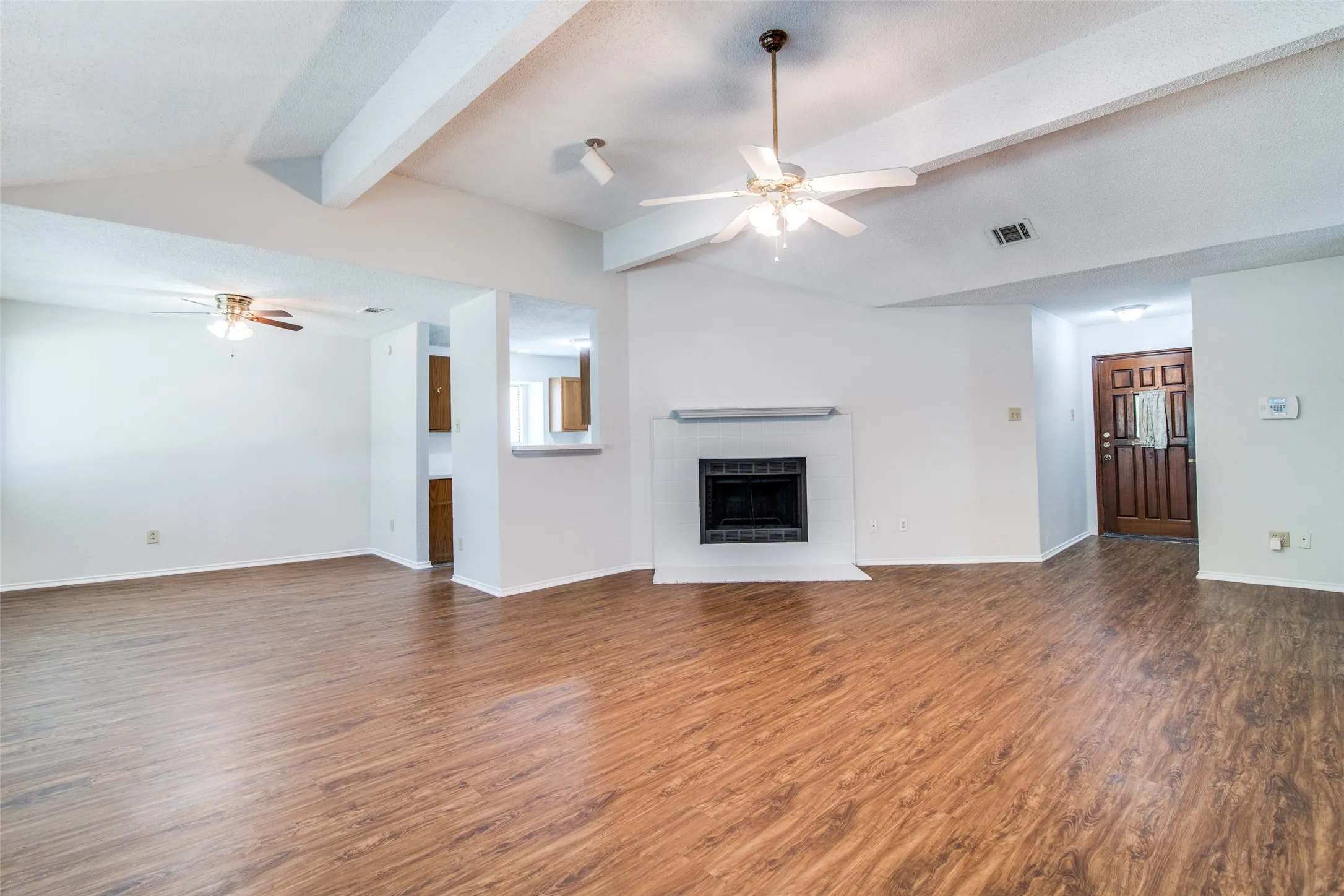 Vaulted ceiling with exposed beams, wood-finish flooring, fireplace with white mantel, ceiling fans, and a paneled entry door