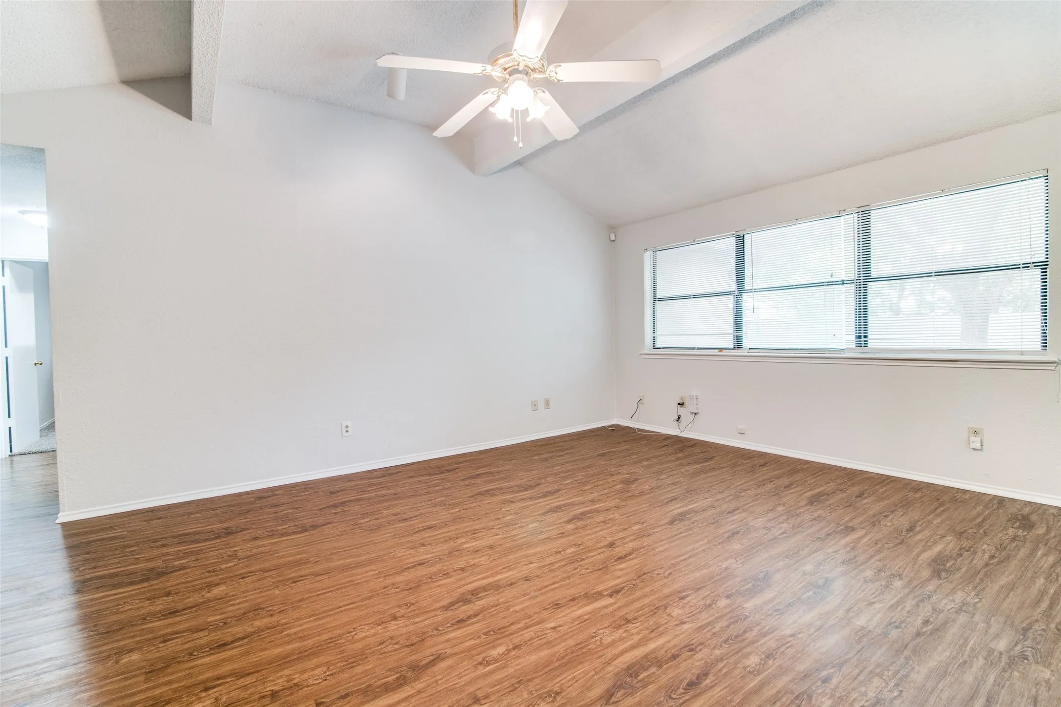 Vaulted ceiling, wood-finish flooring, ceiling fan with light fixture, and multiple windows with blinds