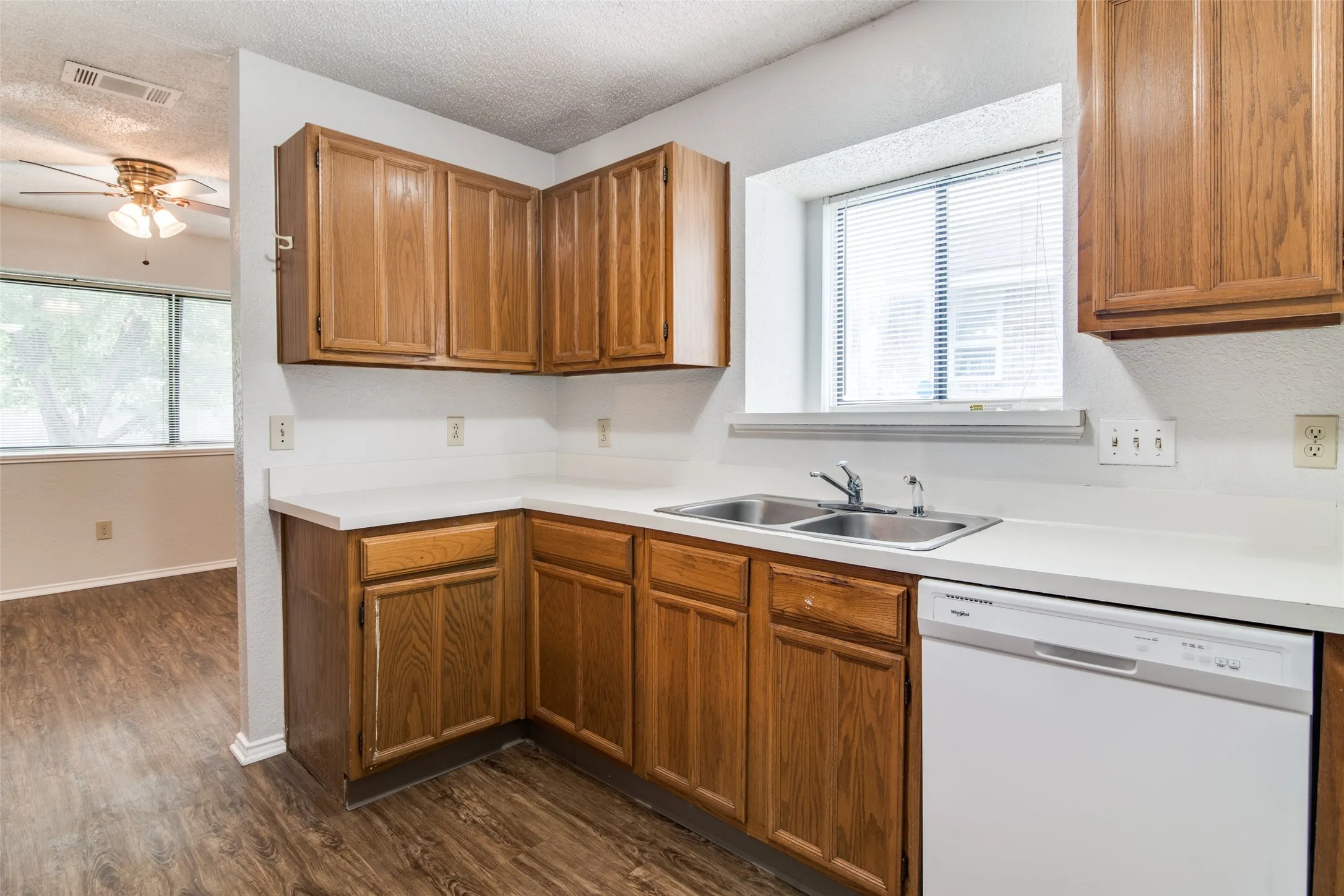 Kitchen featuring wood-finish cabinetry, white countertops, a double basin stainless steel sink, and a white dishwasher