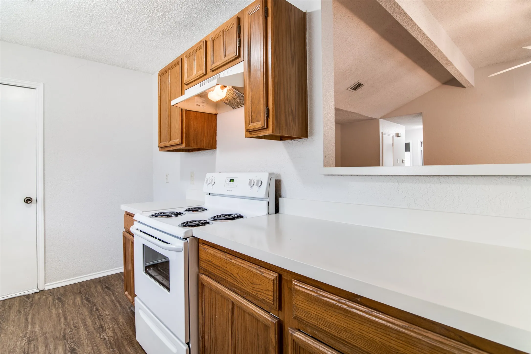 White electric range with coordinating hood, wood-finish cabinetry, light-toned countertops, and wood-finish flooring