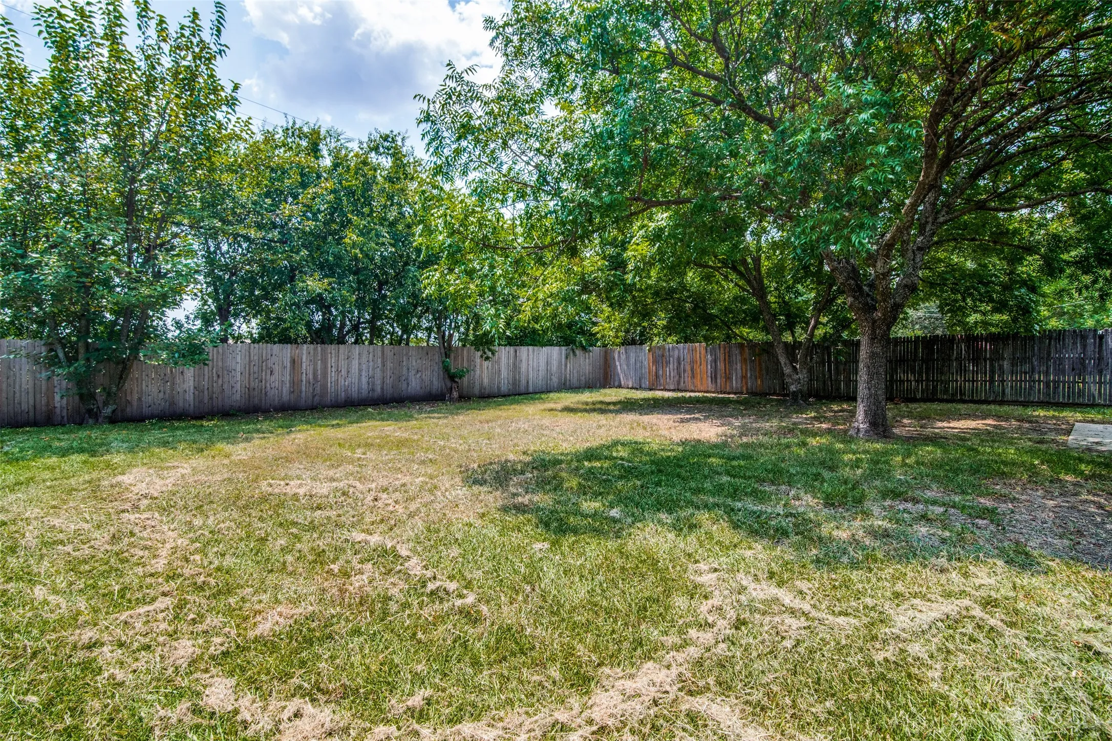 Expansive backyard featuring mature trees and a privacy fence