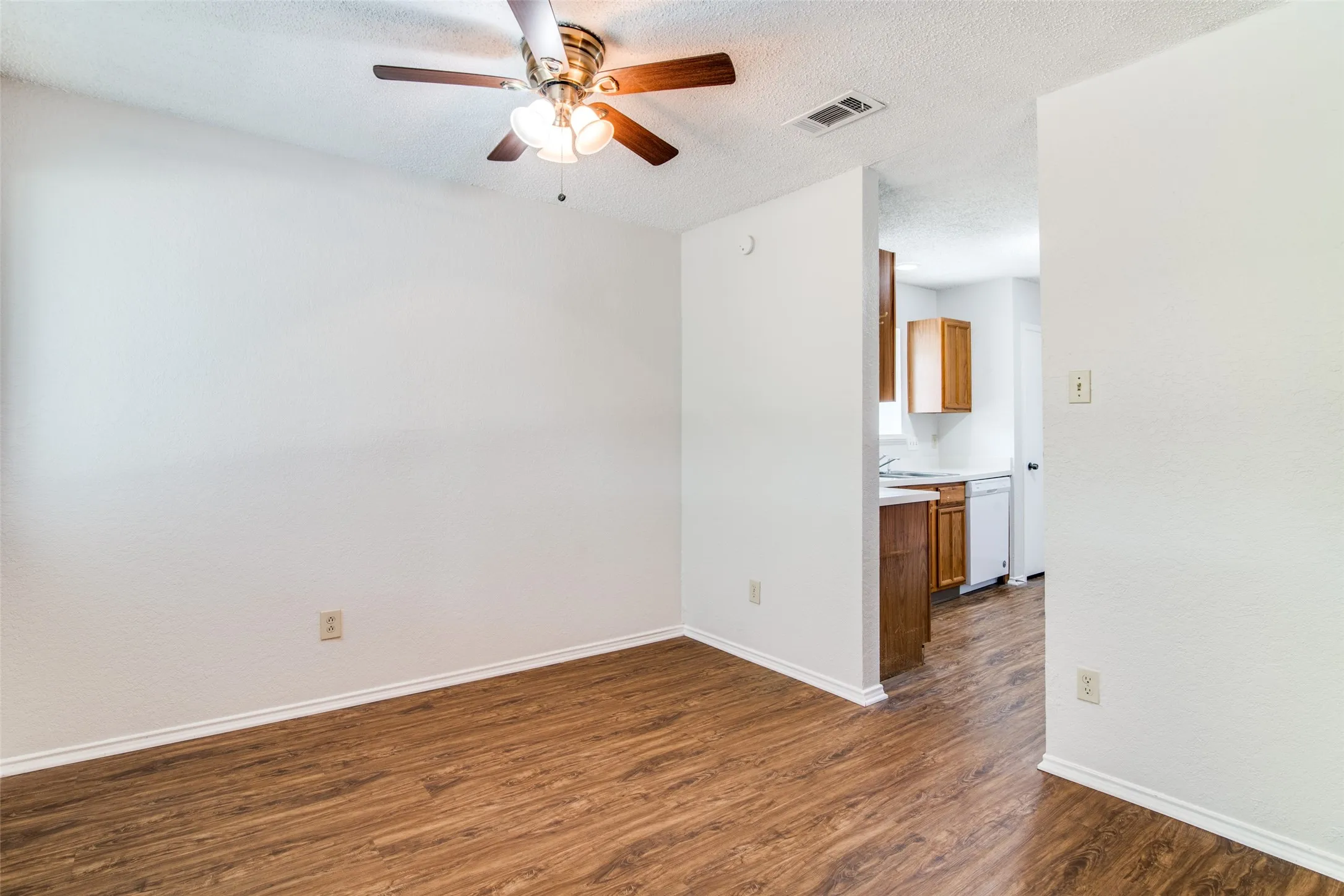 Wood-finish flooring, ceiling fan with integrated lighting, and a partial kitchen with wood cabinetry and white appliances