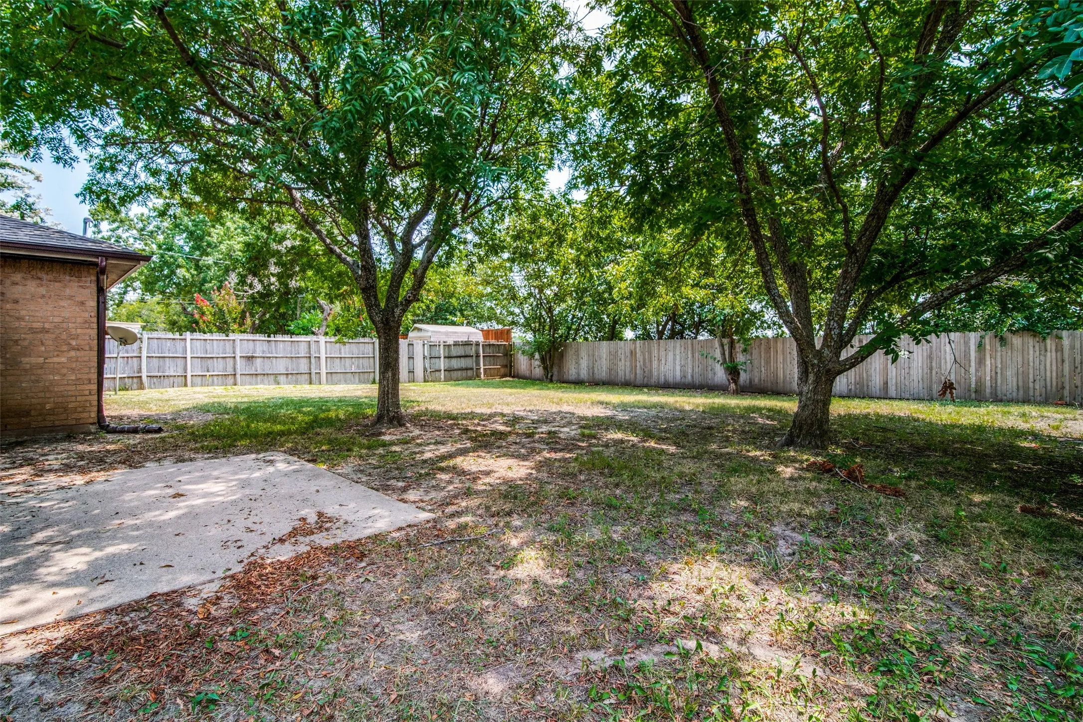 Expansive backyard featuring mature trees, a concrete patio, and a wood privacy fence