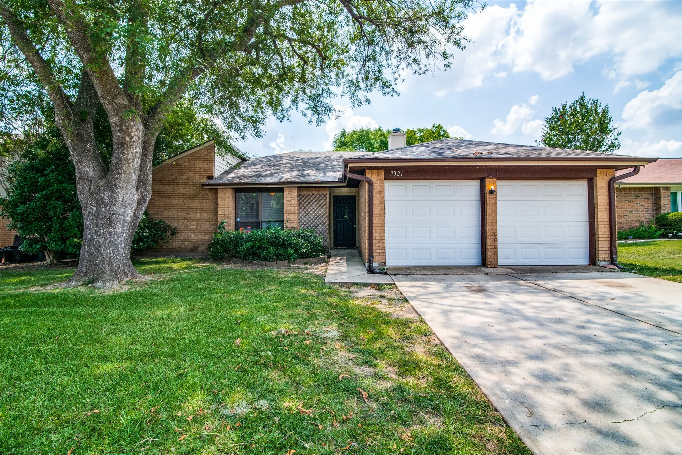 Brick exterior with a pitched roof, attached two-car garage, concrete driveway, and mature landscaping