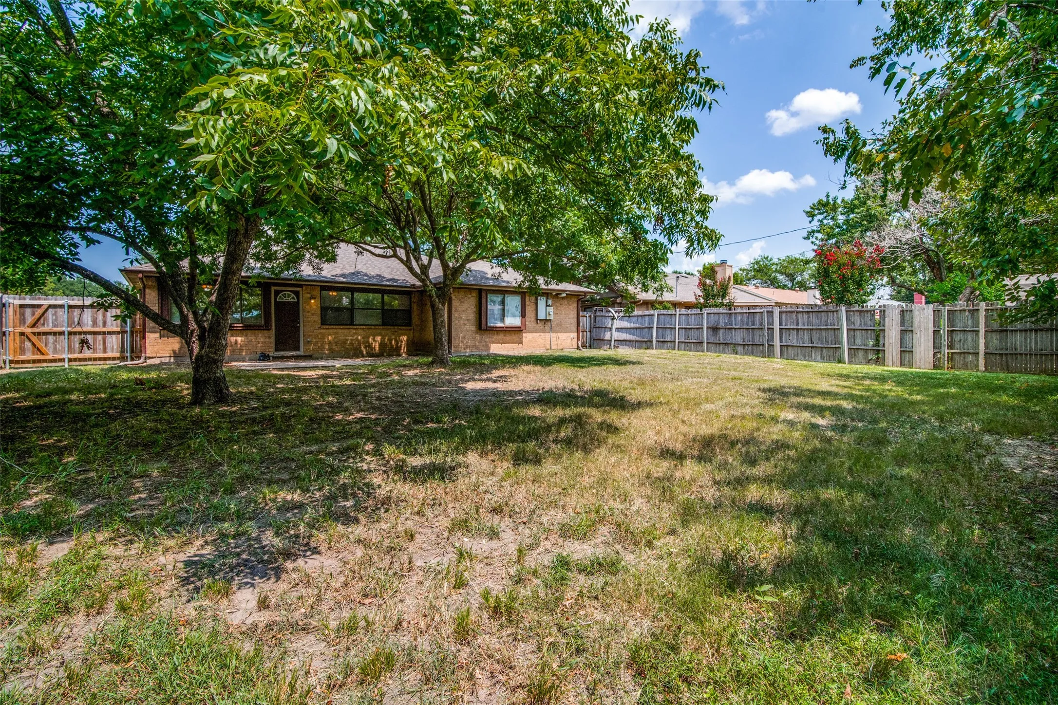 Brick exterior, mature trees, fenced perimeter, covered entry, and dark-framed windows