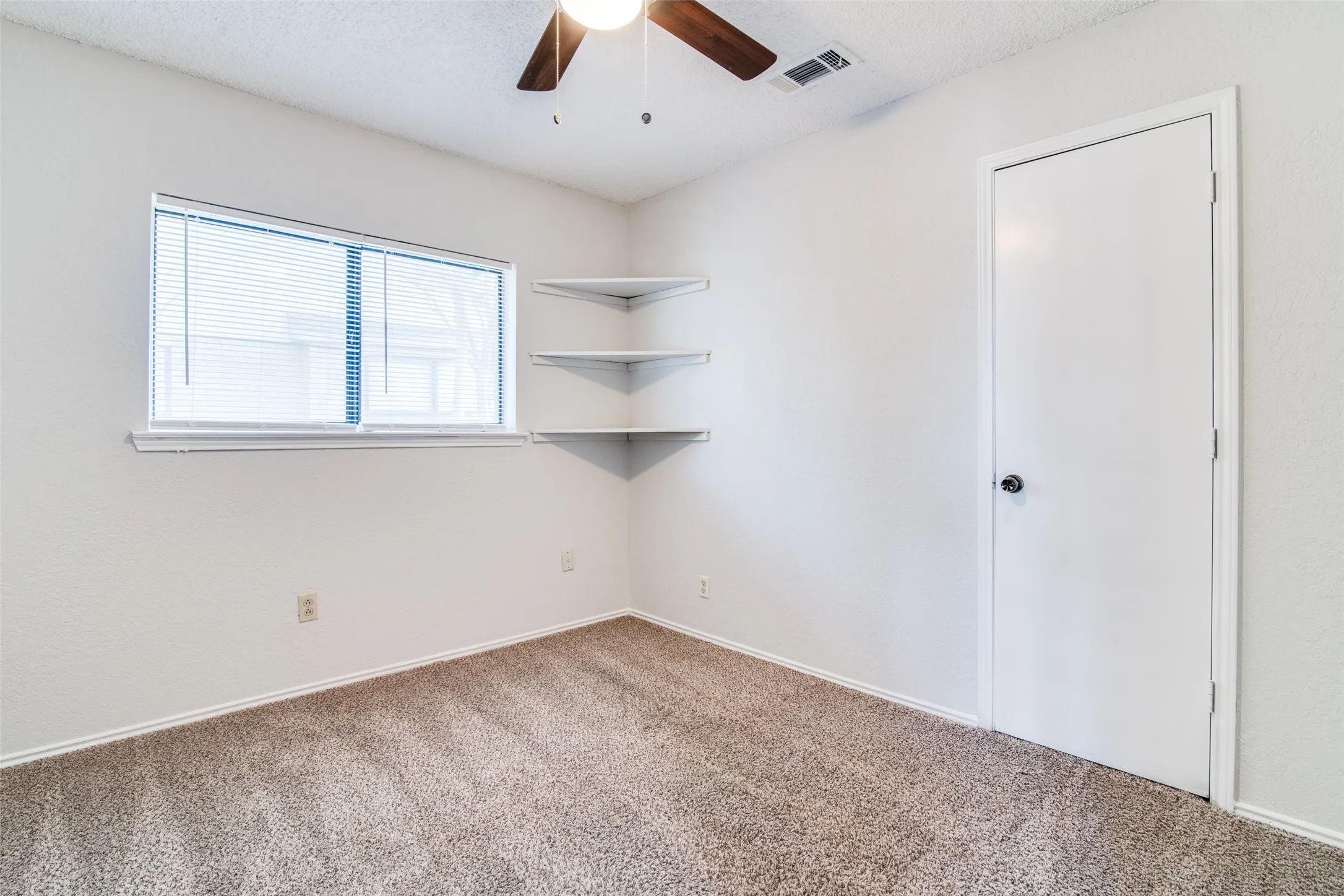 Recessed window with blinds, built-in corner shelving, overhead ceiling fan with light fixture, and carpeted flooring