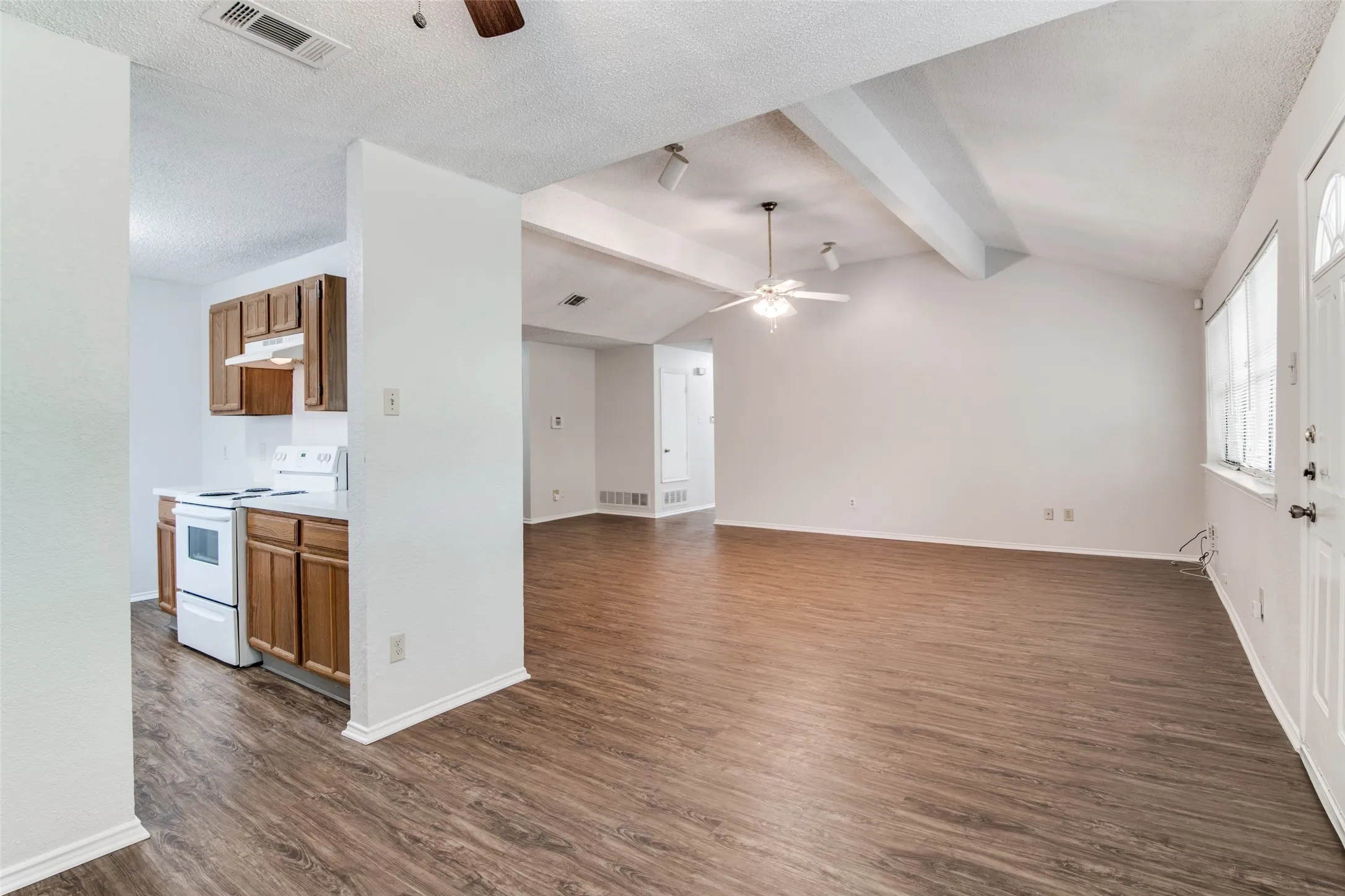 Open-concept living area with wood-finish flooring, vaulted ceiling, and exposed beams
