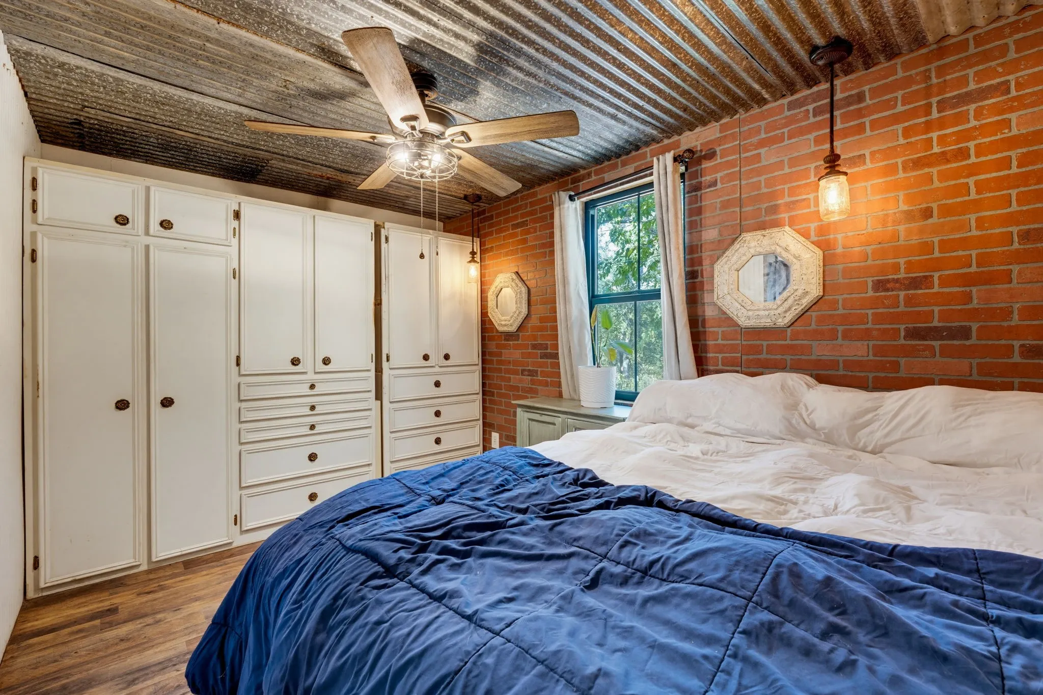 Corrugated metal ceiling, exposed brick wall, wood-finish flooring, built-in cabinetry, and ceiling fan with integrated lighting