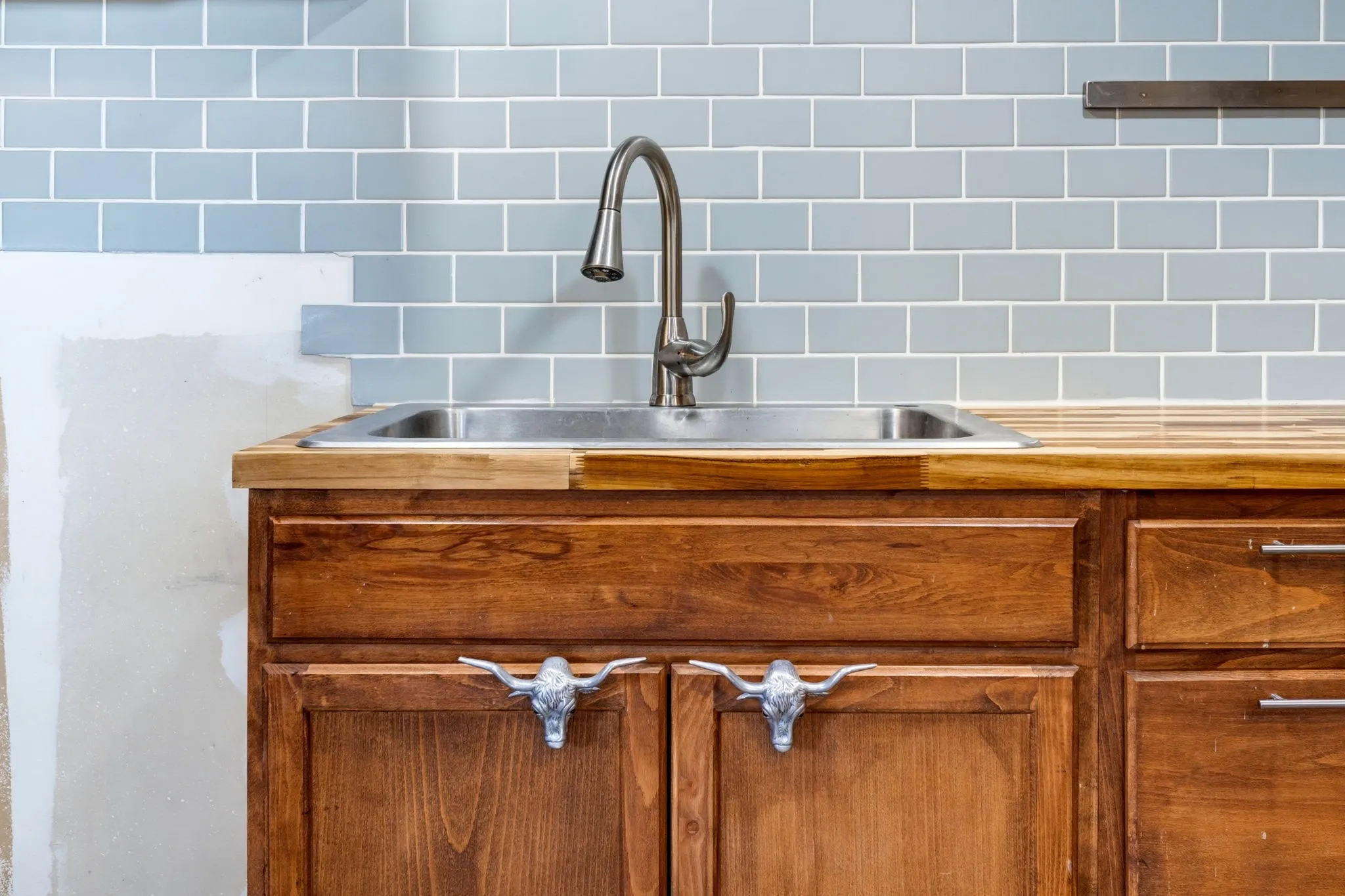 Wood cabinetry with custom longhorn hardware, stainless steel sink, gooseneck faucet, and butcher block countertop