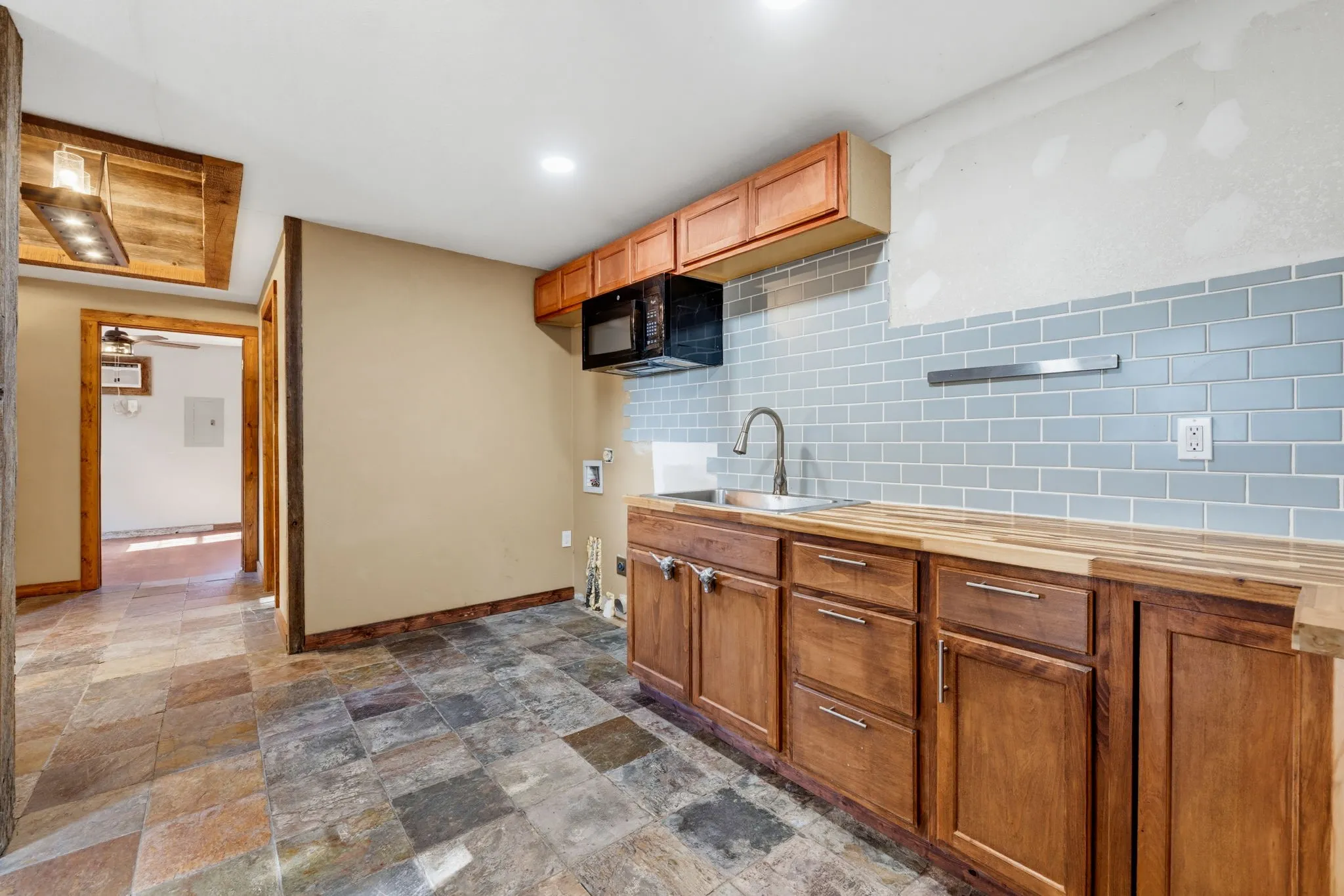 Full kitchen featuring wood cabinetry, butcher block countertops, a stainless steel sink, a microwave, and subway tile backsplash