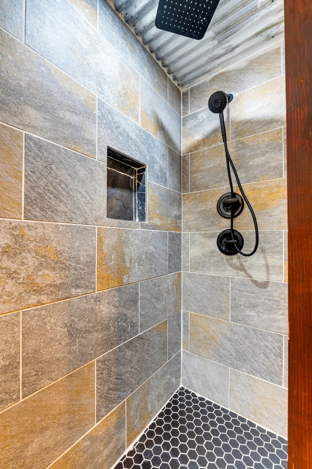 Tiled shower featuring a built-in niche, matte black shower fixtures, corrugated ceiling, and hexagonal floor tile