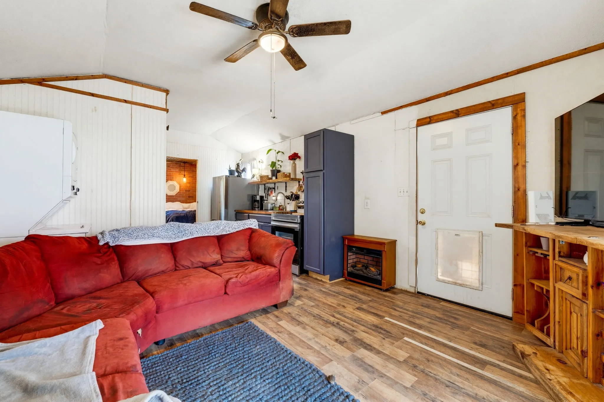 Wood-finish flooring throughout, featuring a ceiling fan with light fixture, built-in shelving, and a white entry door