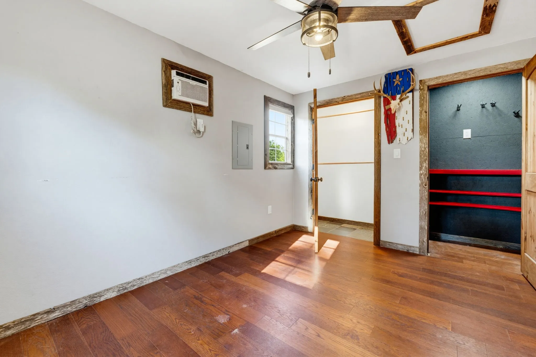 Wood-finish flooring, ceiling fan with integrated lighting, window-mounted air conditioning unit, and built-in shelving