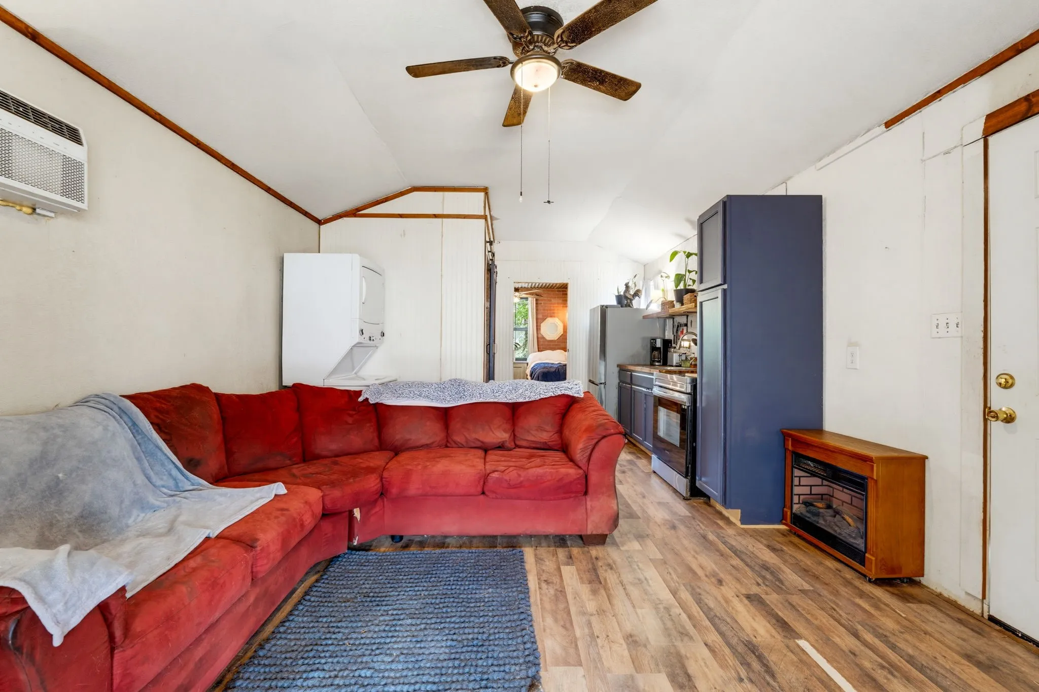 Wood-finish flooring, built-in ceiling fan, white paneled walls, and partial kitchen with dark cabinetry