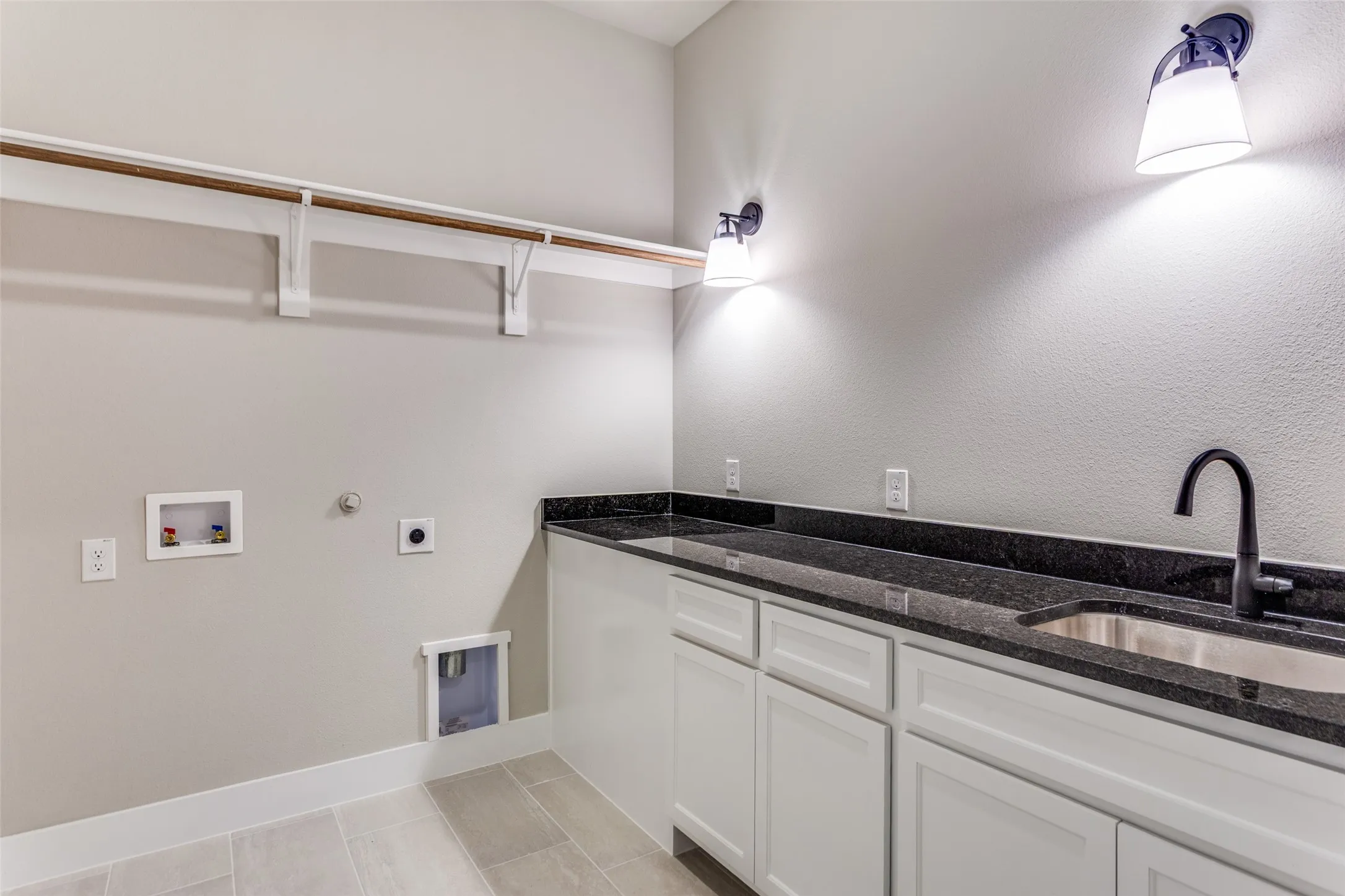 Laundry area featuring a built-in sink with a gooseneck faucet, dark countertops, white cabinetry, and a clothing rod