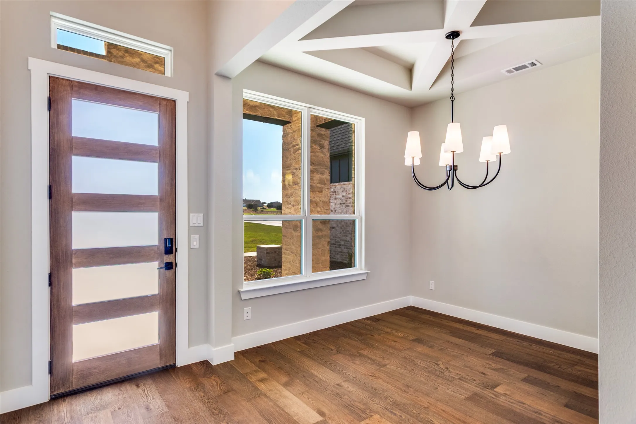 Wood-finish flooring, contemporary chandelier, coffered ceiling, transom window, and a modern entry door with frosted glass panels