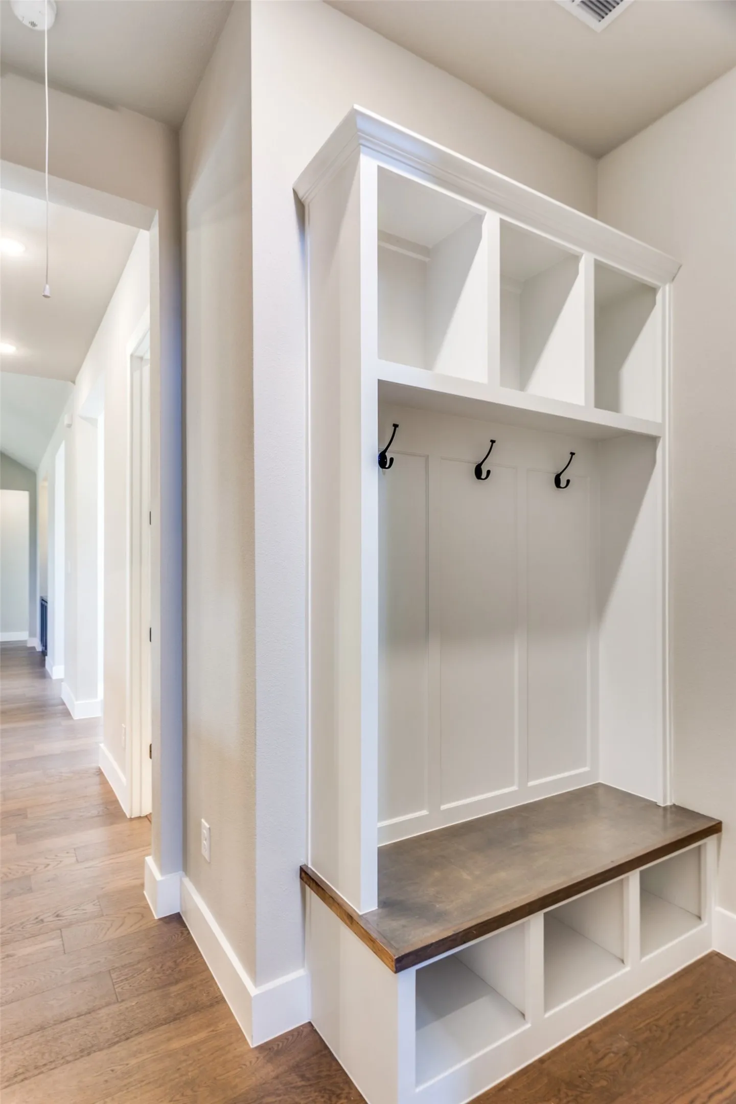 Built-in hall tree with storage cubbies, bench seating, integrated hooks, and upper shelving, complemented by wood-finish flooring