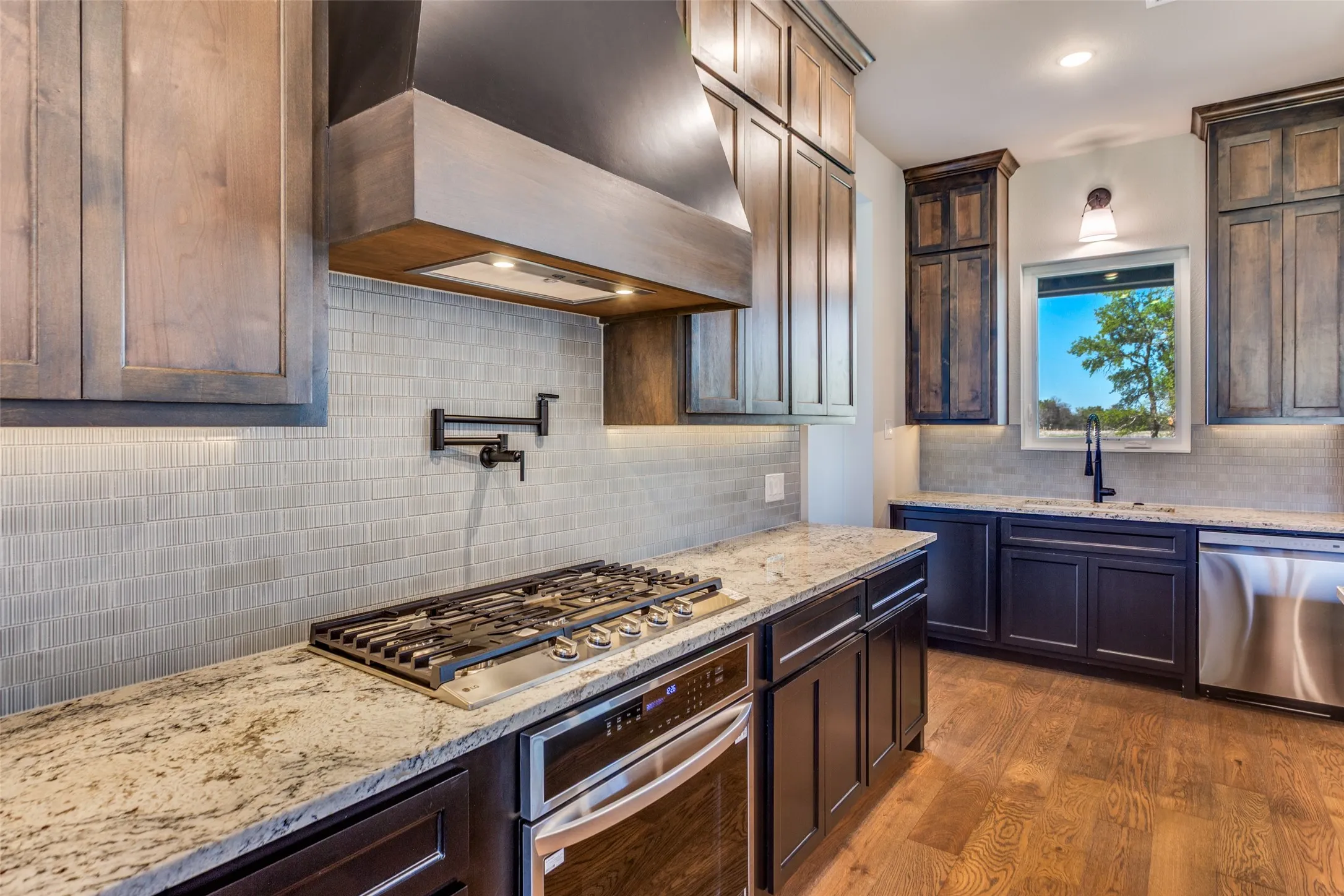 Gourmet kitchen featuring a built-in gas range, stainless steel appliances, granite countertops, tile backsplash, and wood-finish flooring
