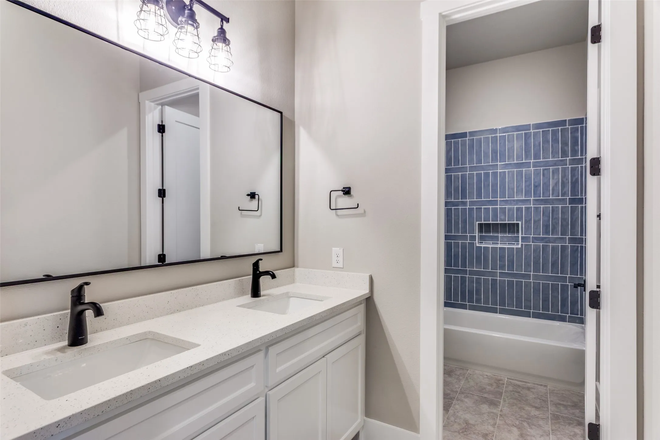 Dual-sink vanity with quartz countertop, matte black faucets, and an expansive framed mirror