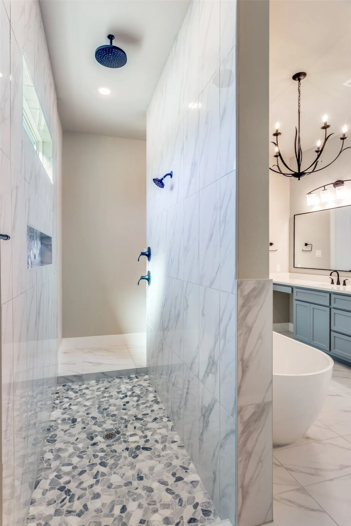 Walk-in shower with a rain shower head, pebble-tile flooring, and marble-finish wall tiling