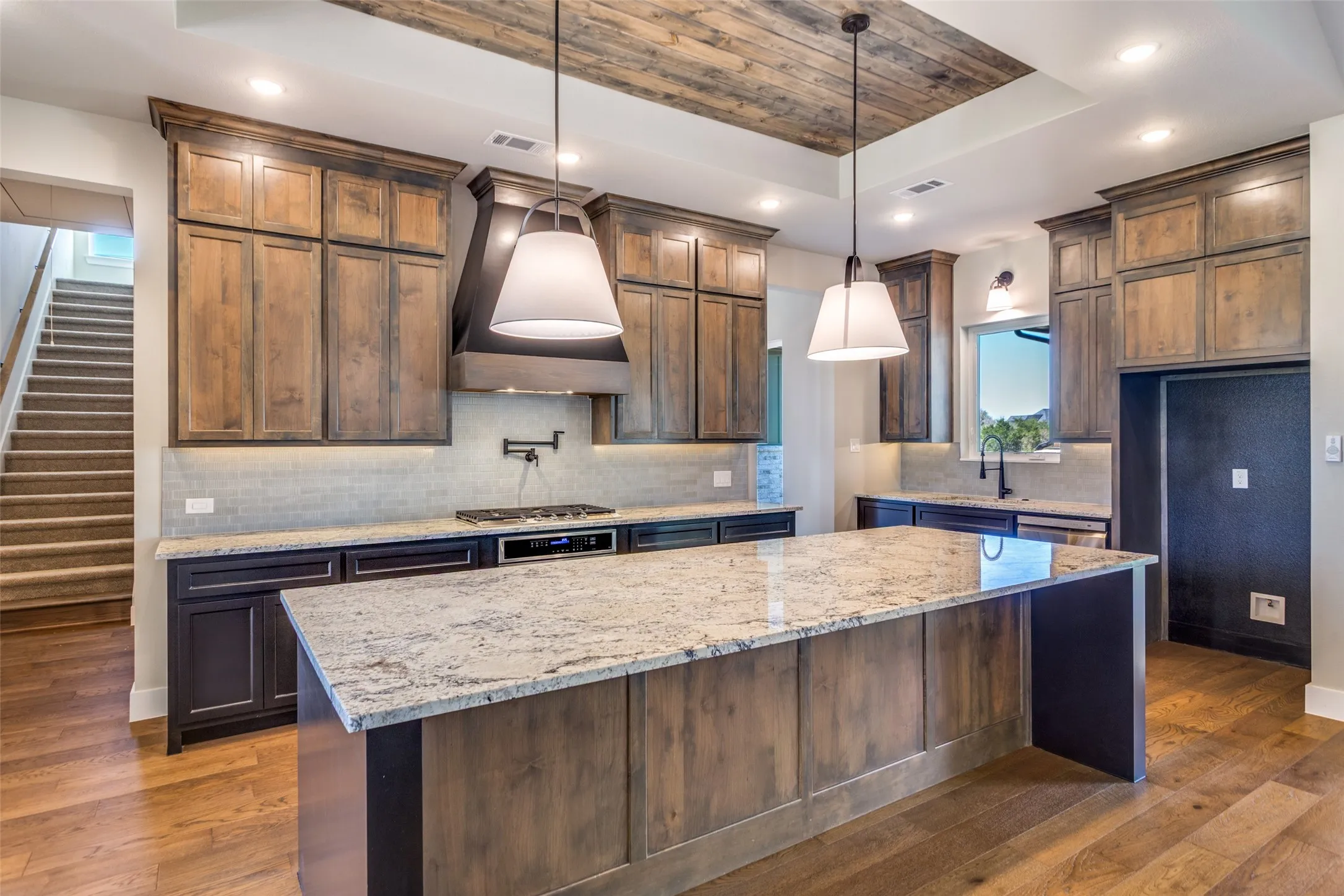 Kitchen featuring a wood-finish ceiling accent, large center island with stone countertop, wood-finish cabinetry, and stainless-steel appliances
