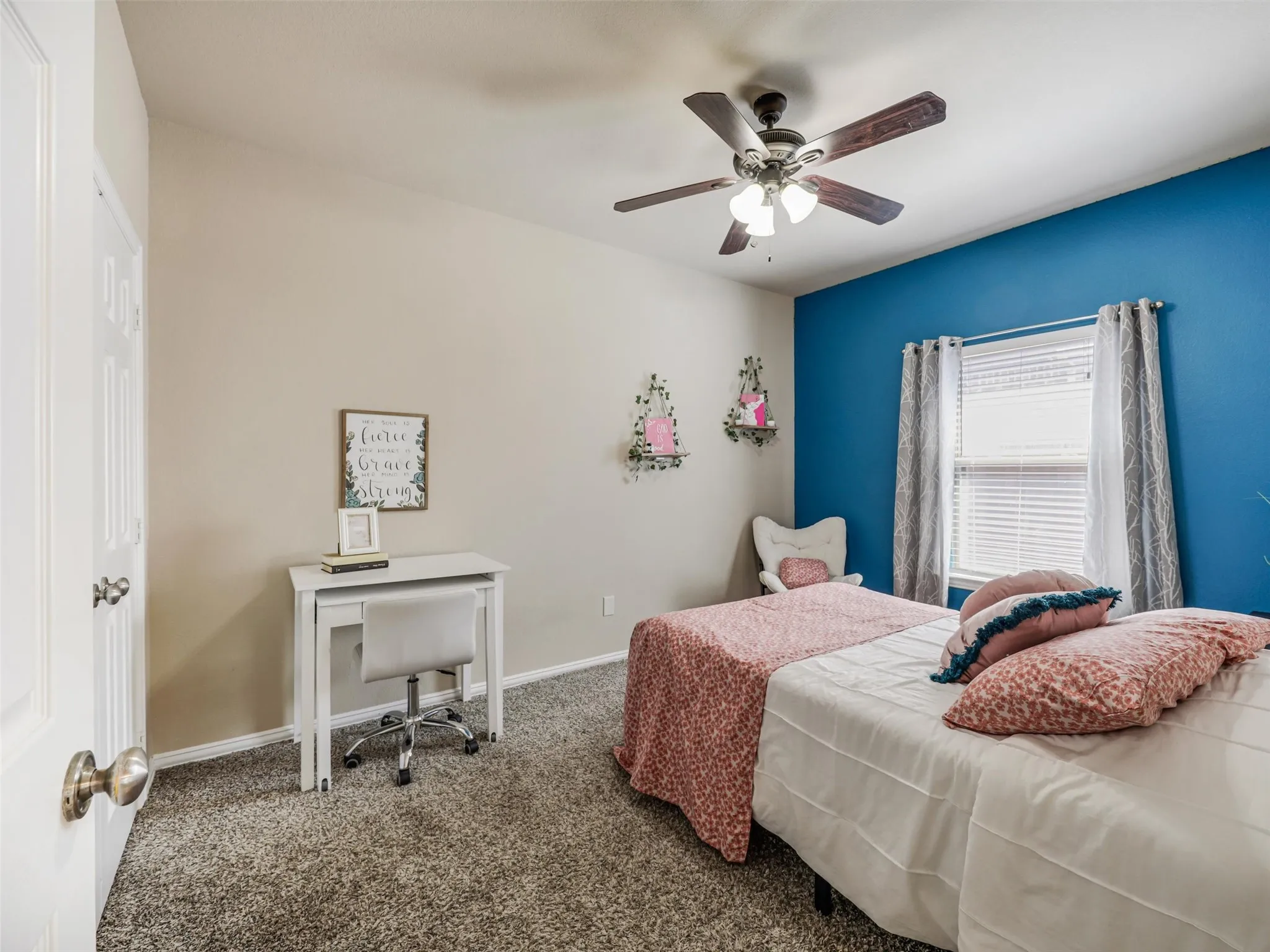 Spacious secondary bedroom features a blue accent wall, ceiling fan, and a window overlooking the front yard.