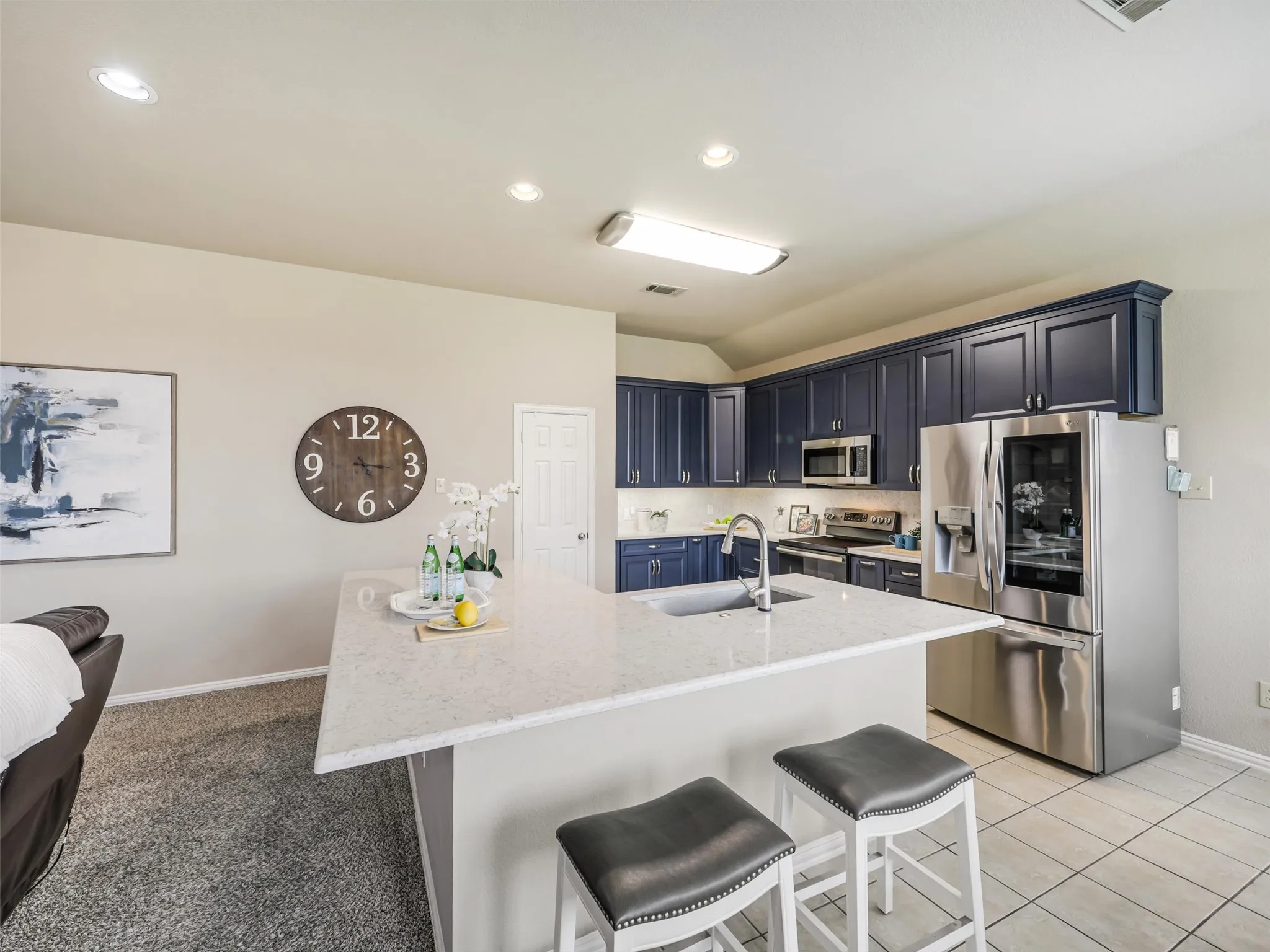 Expansive peninsula offers ample prep space and casual seating, complemented by blue cabinetry, stainless steel appliances, and tile flooring.