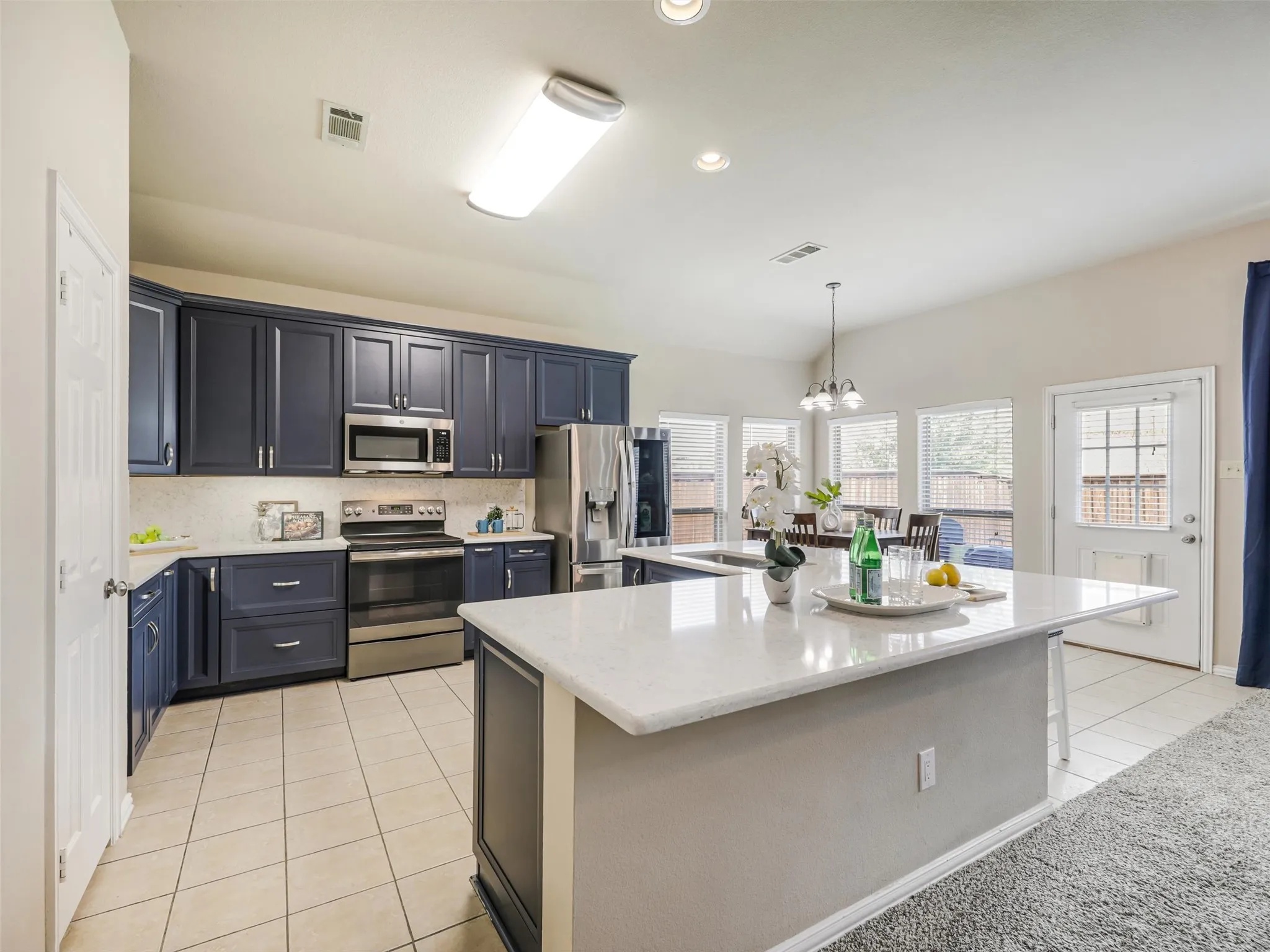 Updated kitchen showcases deep blue cabinetry, quartz countertops, stainless steel appliances, and a generous peninsula overlooking the living room.