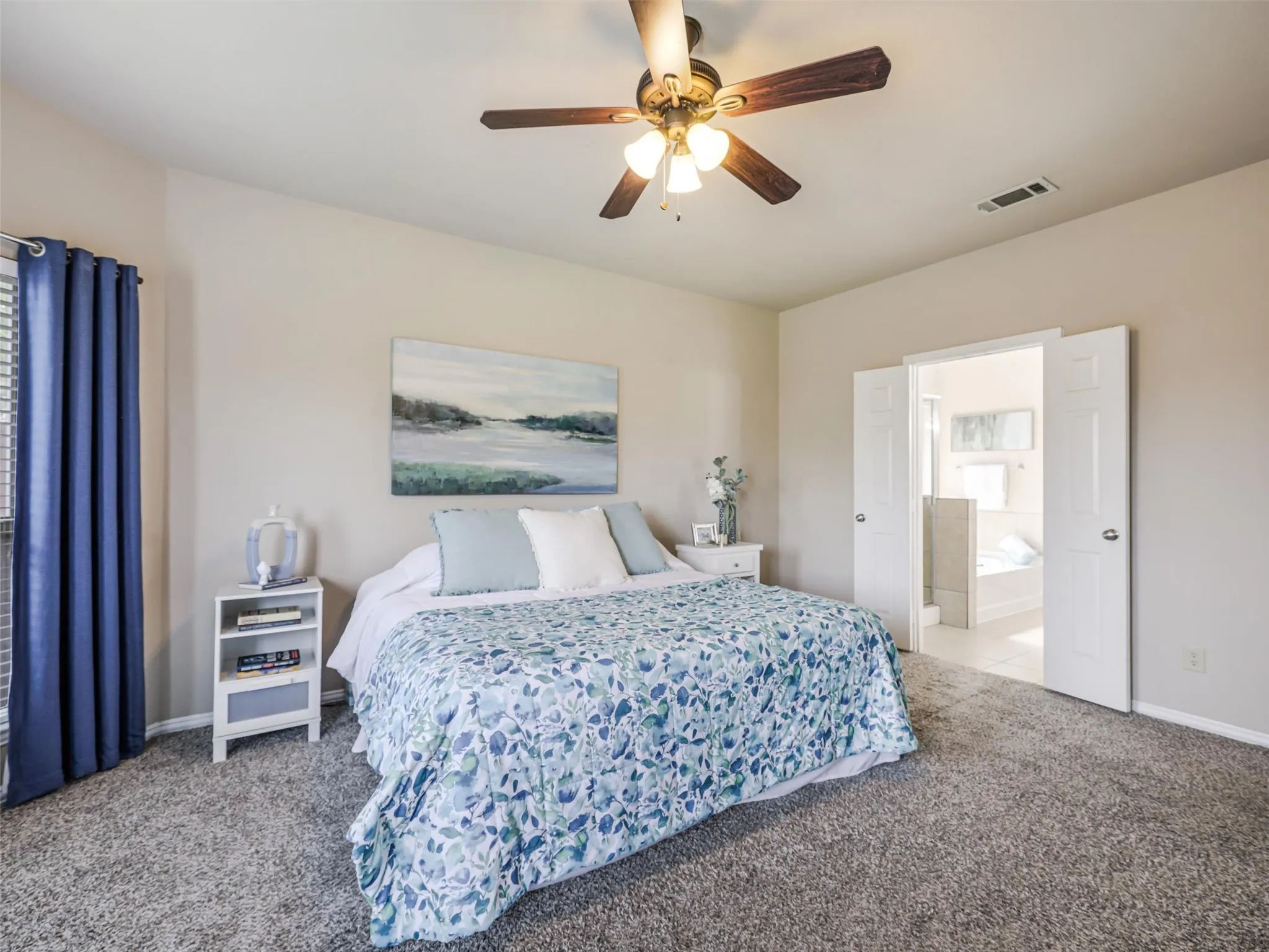 Inviting primary suite features neutral walls, carpeting, and double doors leading to the adjoining private bathroom.