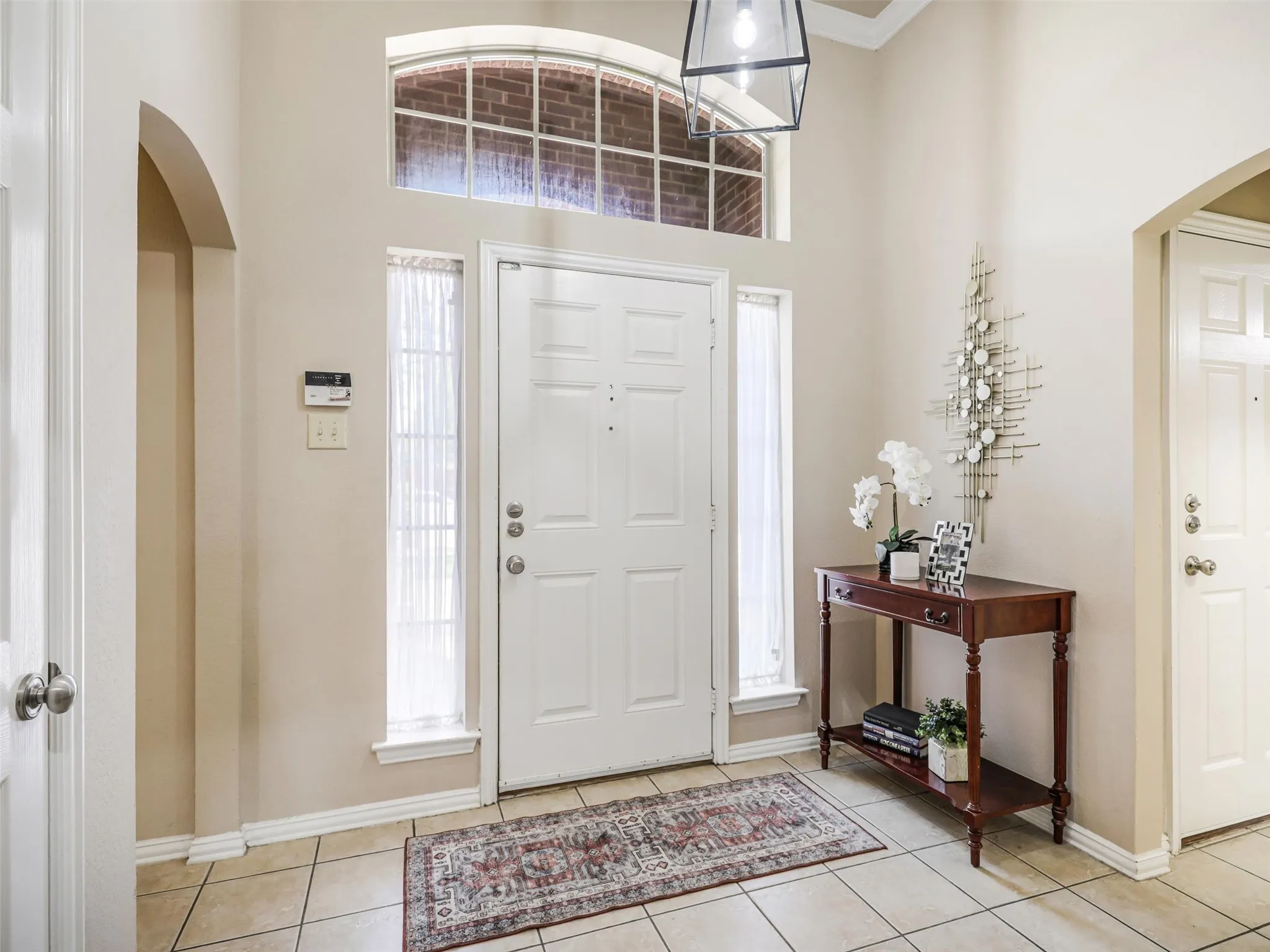 Welcoming foyer features tile flooring, a high ceiling, arched openings, and natural light through sidelights and a transom window.
