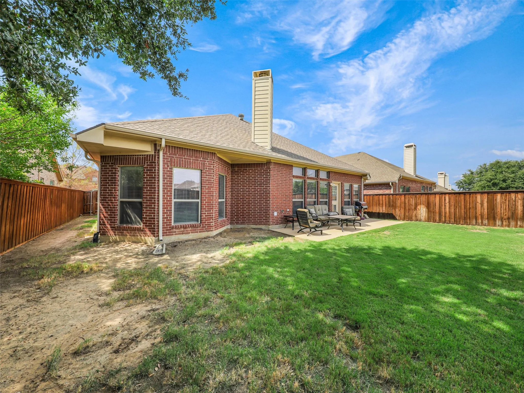 Rear brick exterior features large windows overlooking the backyard and a patio conveniently situated beside the home.