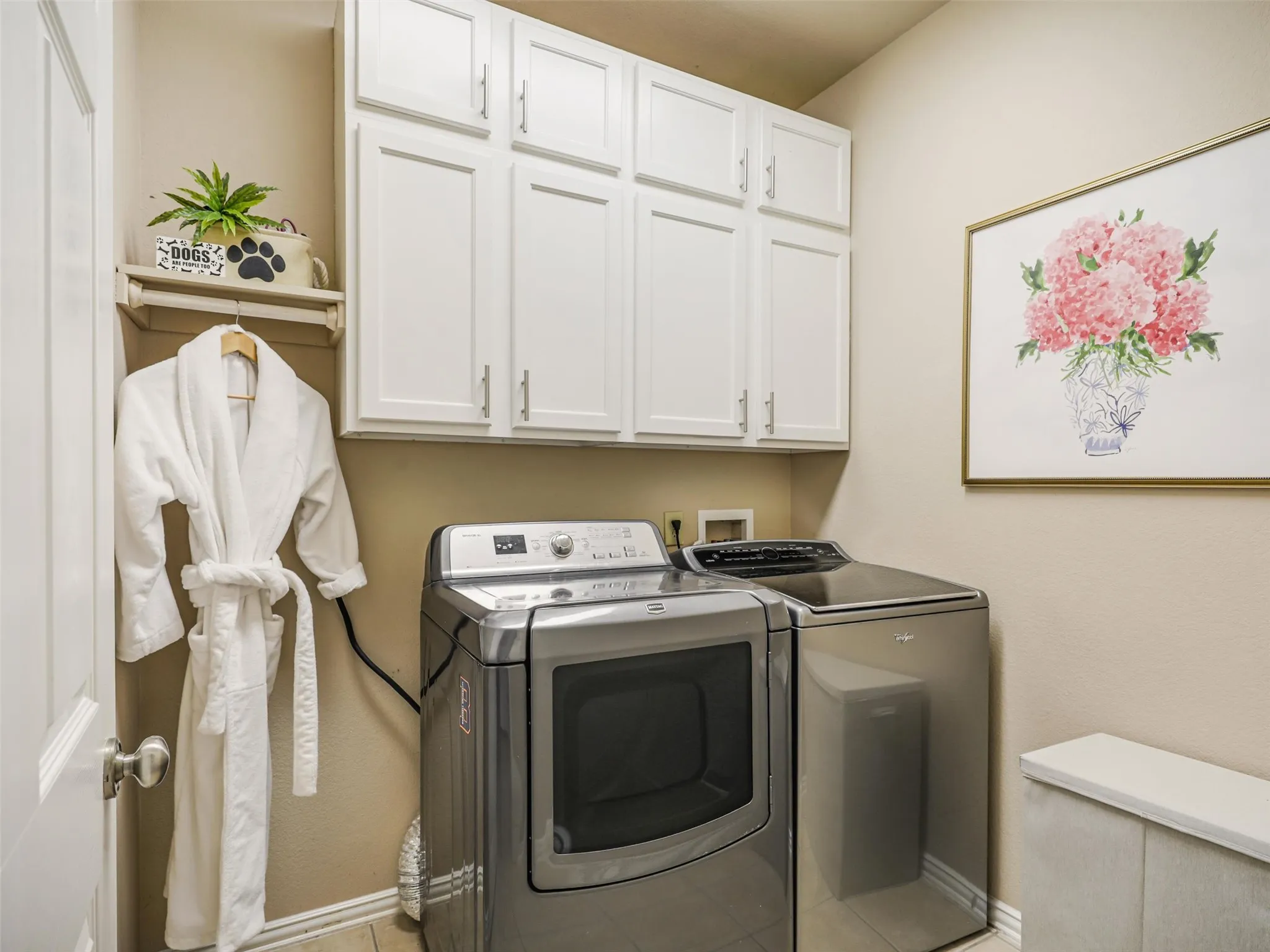 Dedicated laundry room features overhead cabinetry and a hanging rod for convenient storage and organization.