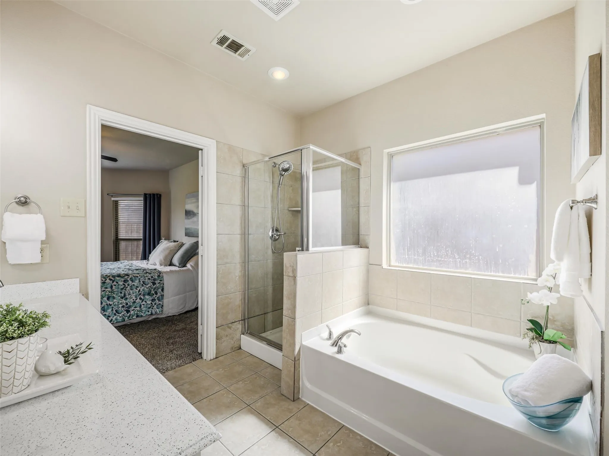 Relax in the soaking tub beneath a large privacy window, complemented by a separate glass-enclosed shower with tile surround.