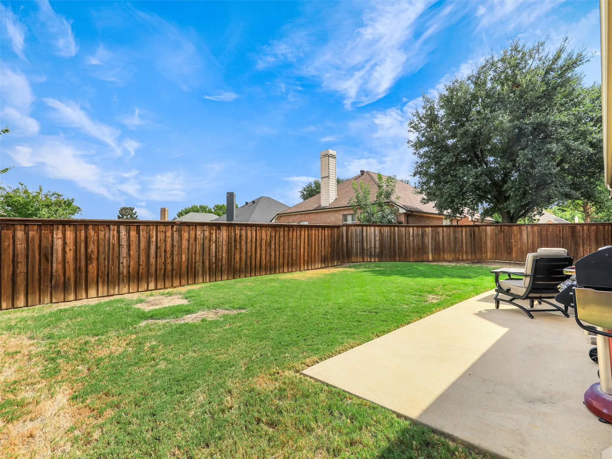 Fenced backyard offers an open lawn and concrete patio with space for outdoor seating, grilling, and relaxing.