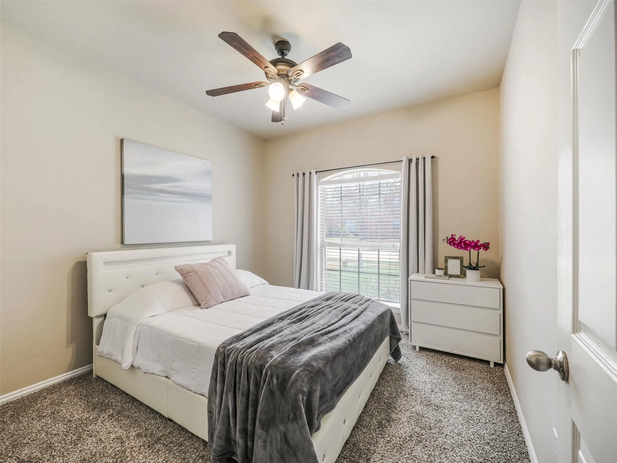 Light-filled secondary bedroom with soft neutral walls, carpeting, and a ceiling fan.