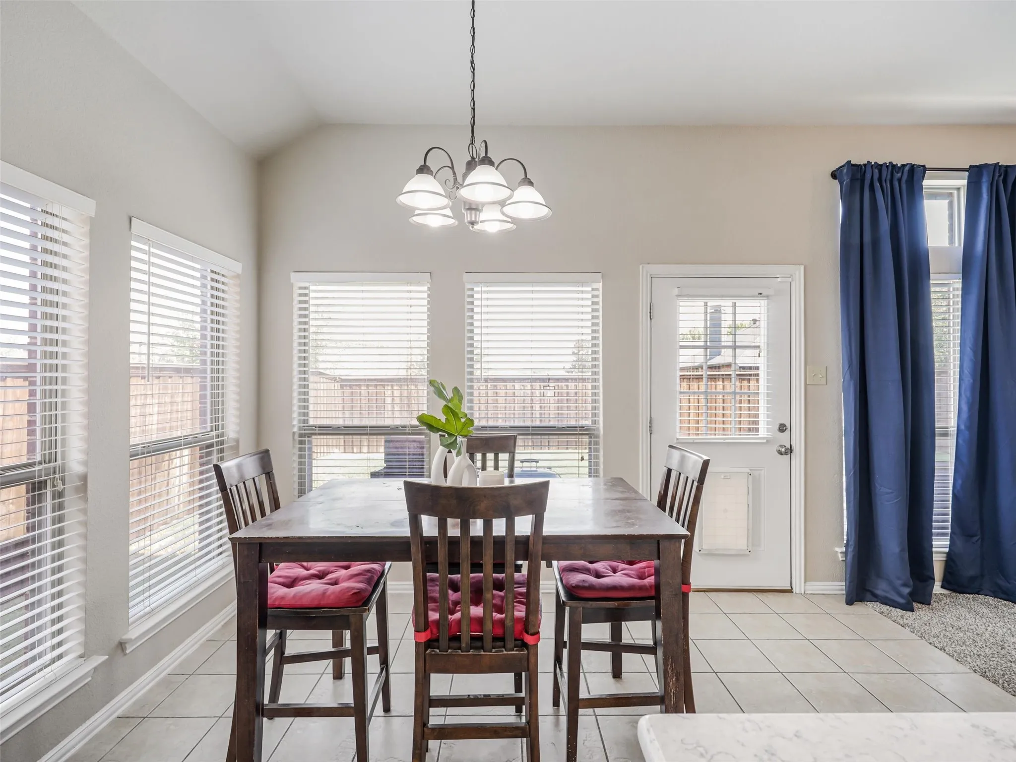Sun-filled breakfast nook features surrounding windows, a decorative chandelier, tile flooring, and direct access to the backyard.