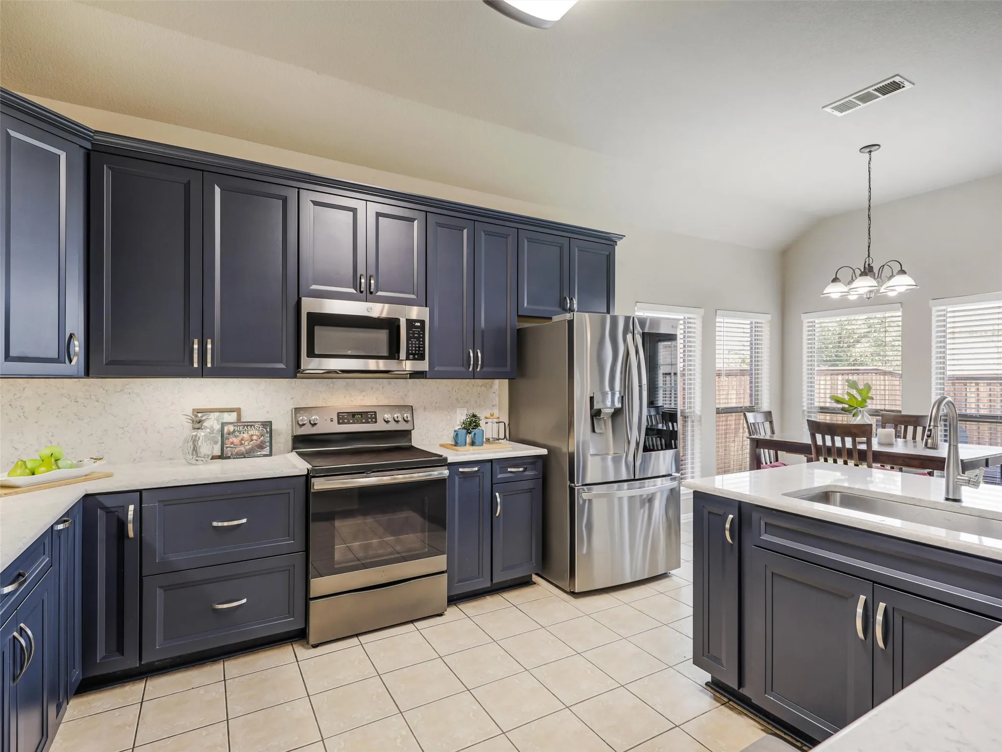 Updated kitchen pairs deep blue cabinetry with light countertops and backsplash, stainless steel appliances, and an adjoining breakfast area.