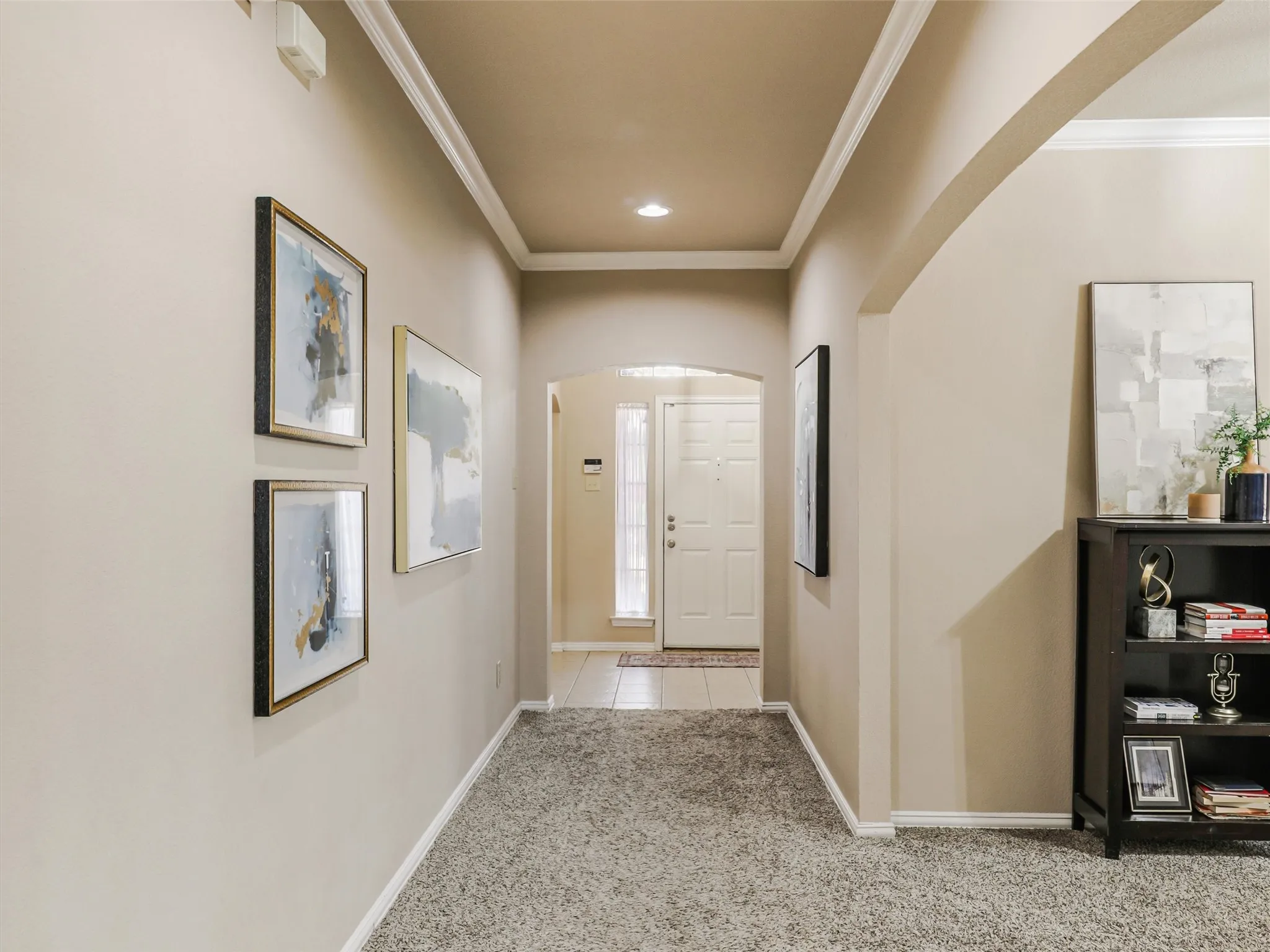 Crown molding, recessed lighting, and arched openings add character to the hallway connecting the front entry with the home’s interior.