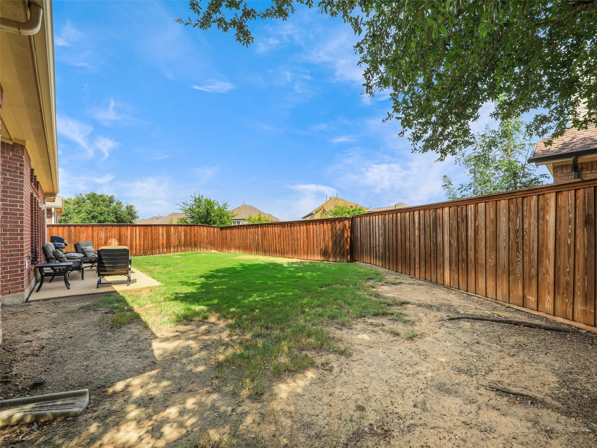 Wide backyard view highlights wood fencing, shade from a mature tree, and room for gardening or outdoor recreation.