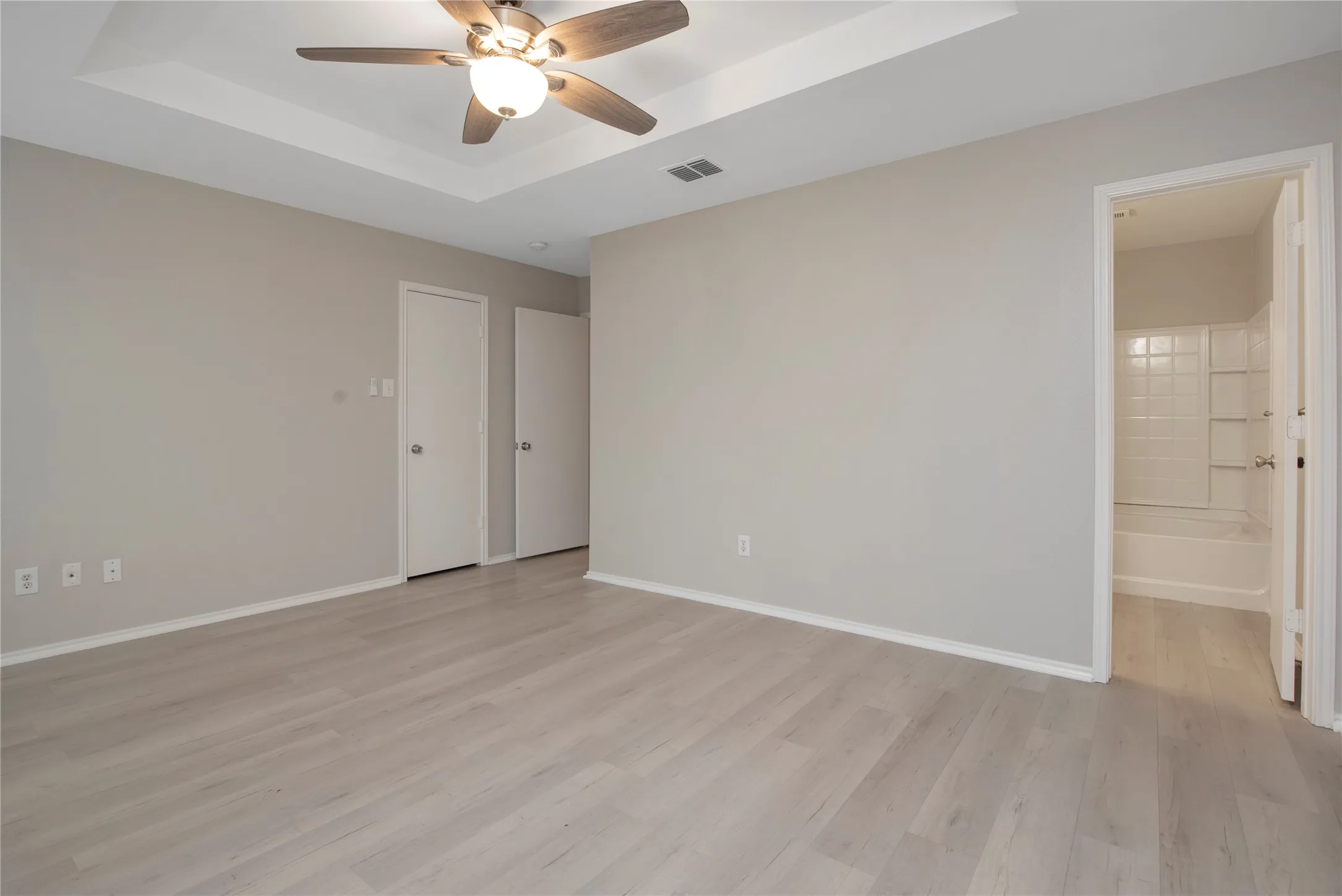 Tray ceiling with a ceiling fan, wood-finish flooring, light neutral wall paint, and white trim
