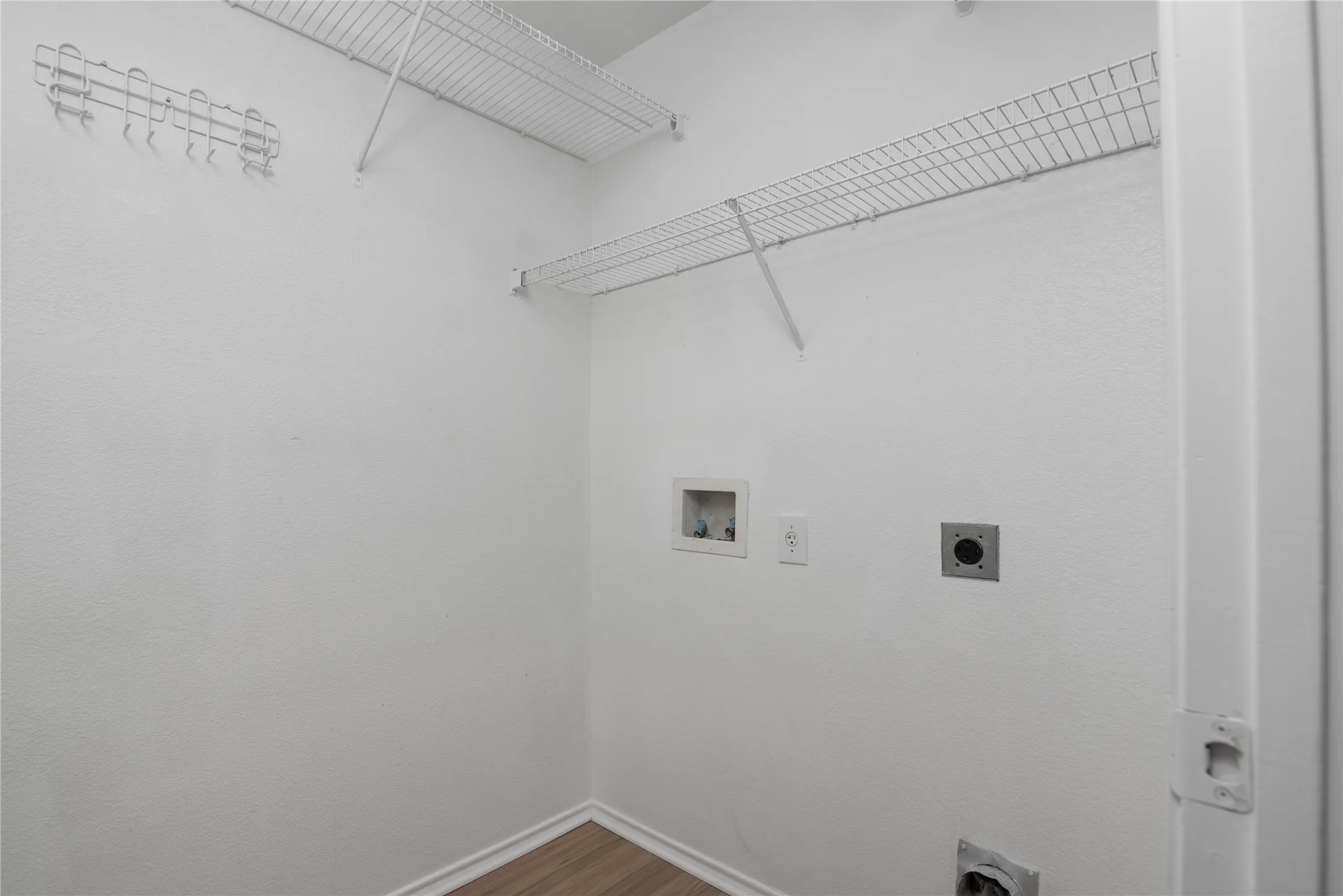 Laundry area featuring wire shelving, utility hookups, and wood-finish flooring