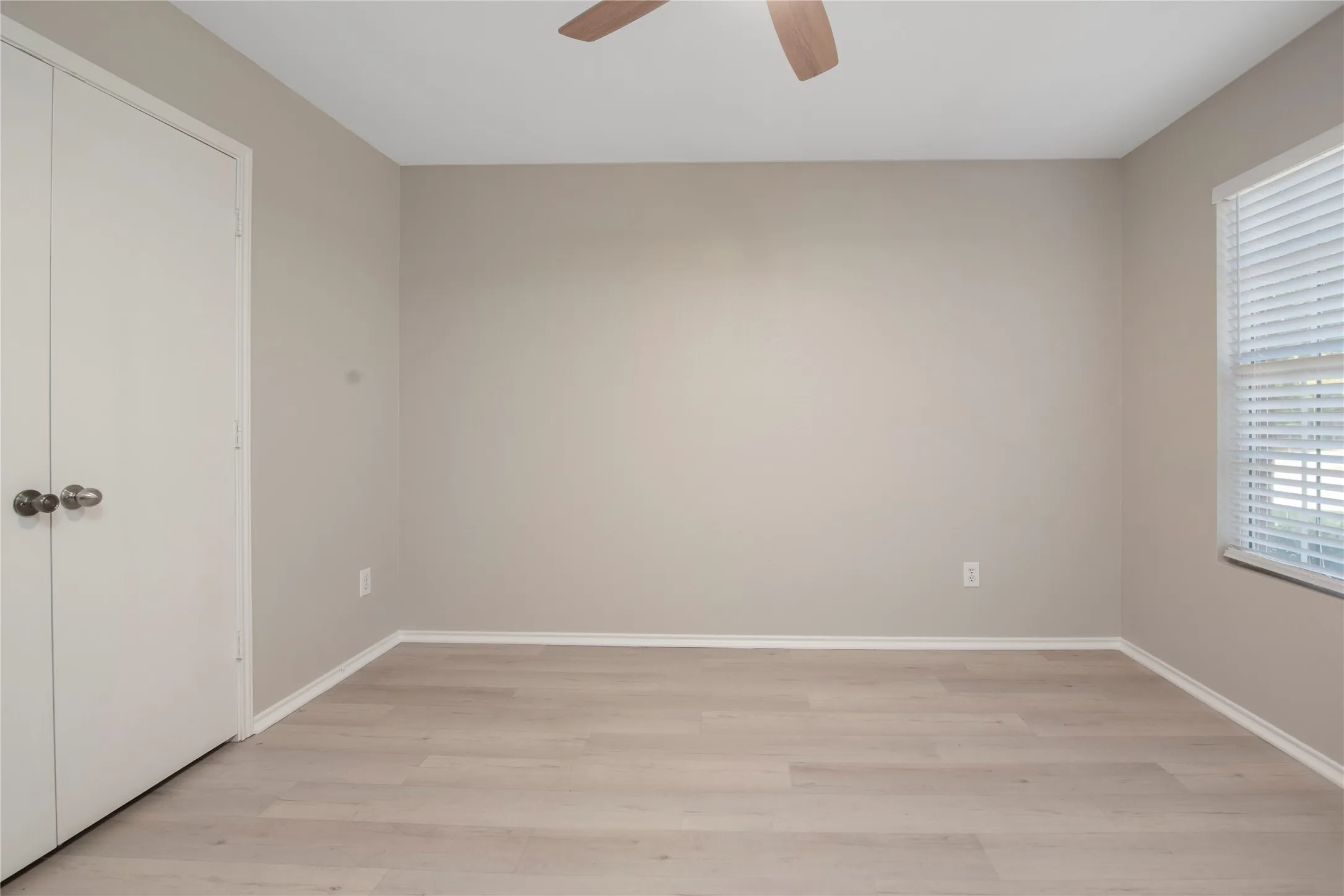 Neutral-toned walls, wood-finish flooring, ceiling fan, and window with blinds