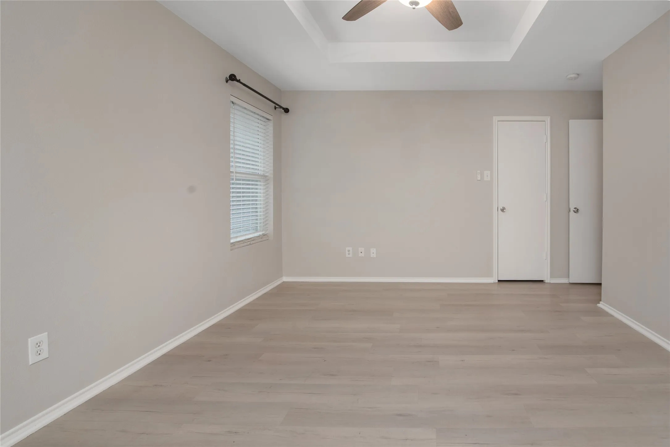 Recessed ceiling with a ceiling fan, light wood-finish flooring, and white trim