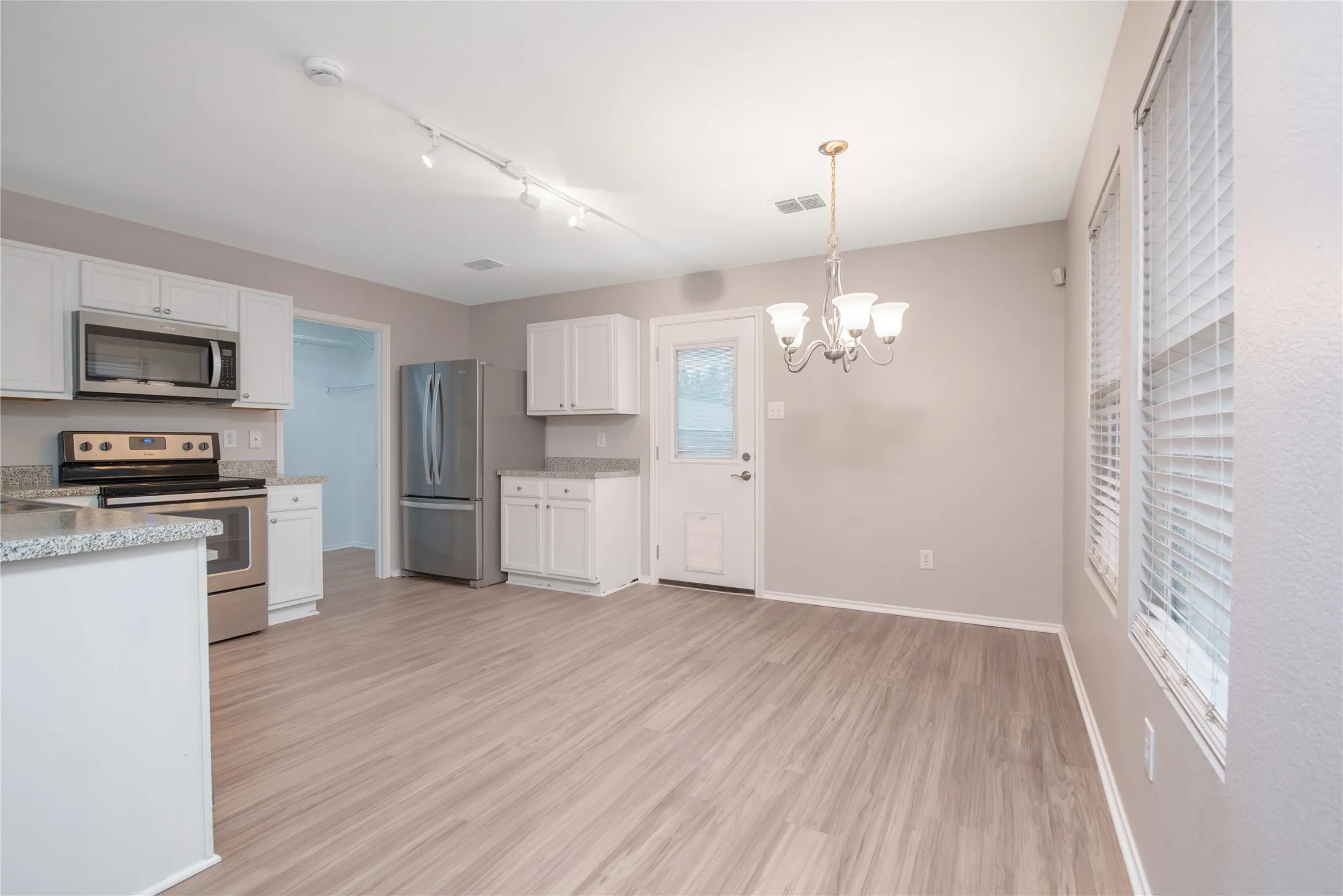 White shaker cabinetry, stainless steel appliances, speckled stone countertops, wood-finish flooring, and a chandelier lighting fixture