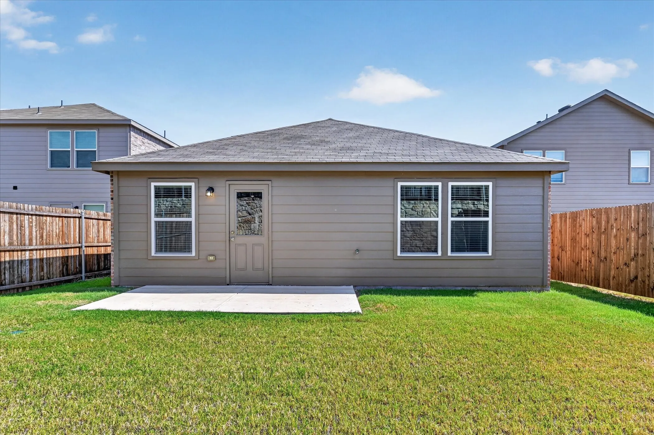 Expansive grassy yard with a concrete patio, wood privacy fencing, and horizontal siding
