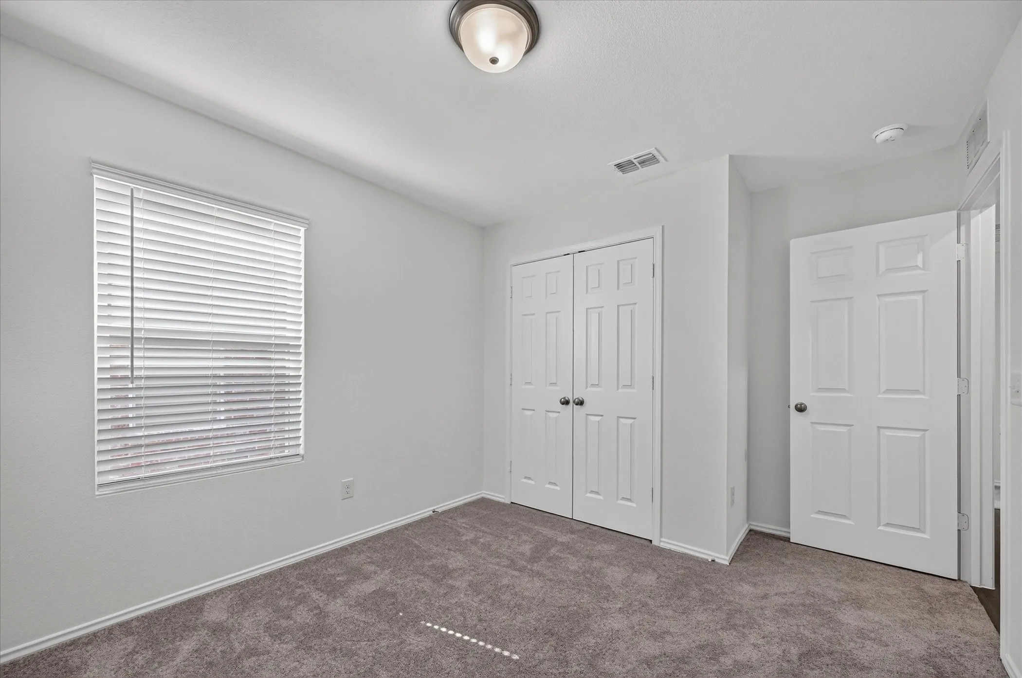 Neutral color palette with textured carpeting, a window with blinds, and white paneled doors