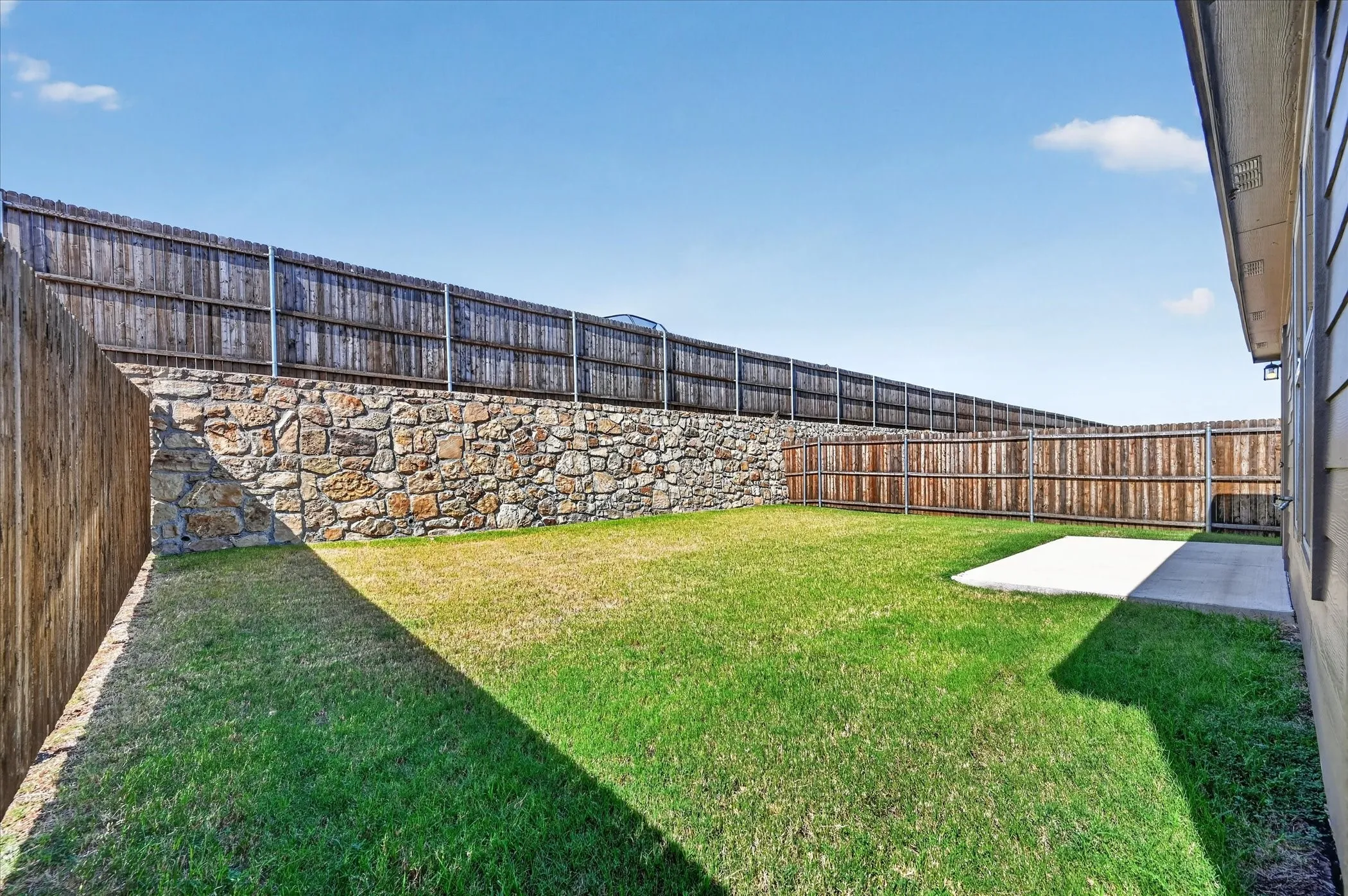 Expansive backyard featuring a manicured lawn, a stone retaining wall, and wood privacy fencing
