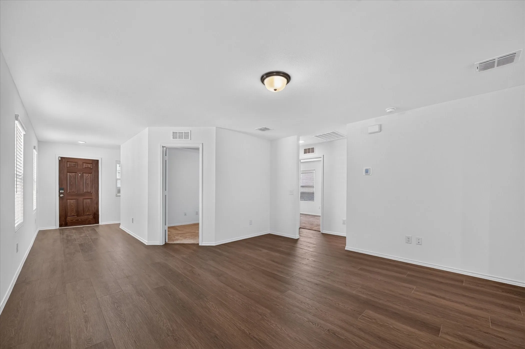 Expansive open-concept living area featuring wood-finish flooring, white painted walls, and a recessed ceiling light fixture