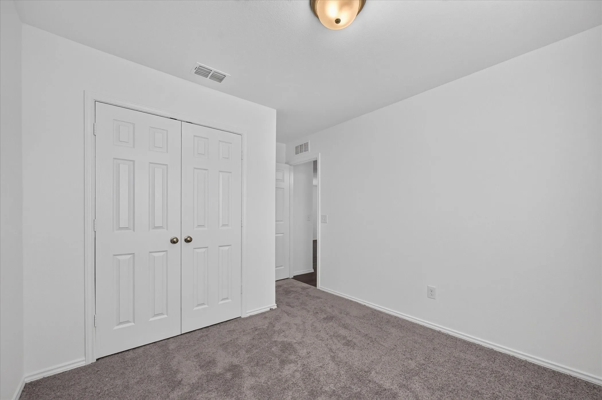 Plush gray carpeting, white painted walls, six-panel bi-fold closet doors, and flush-mount ceiling lighting